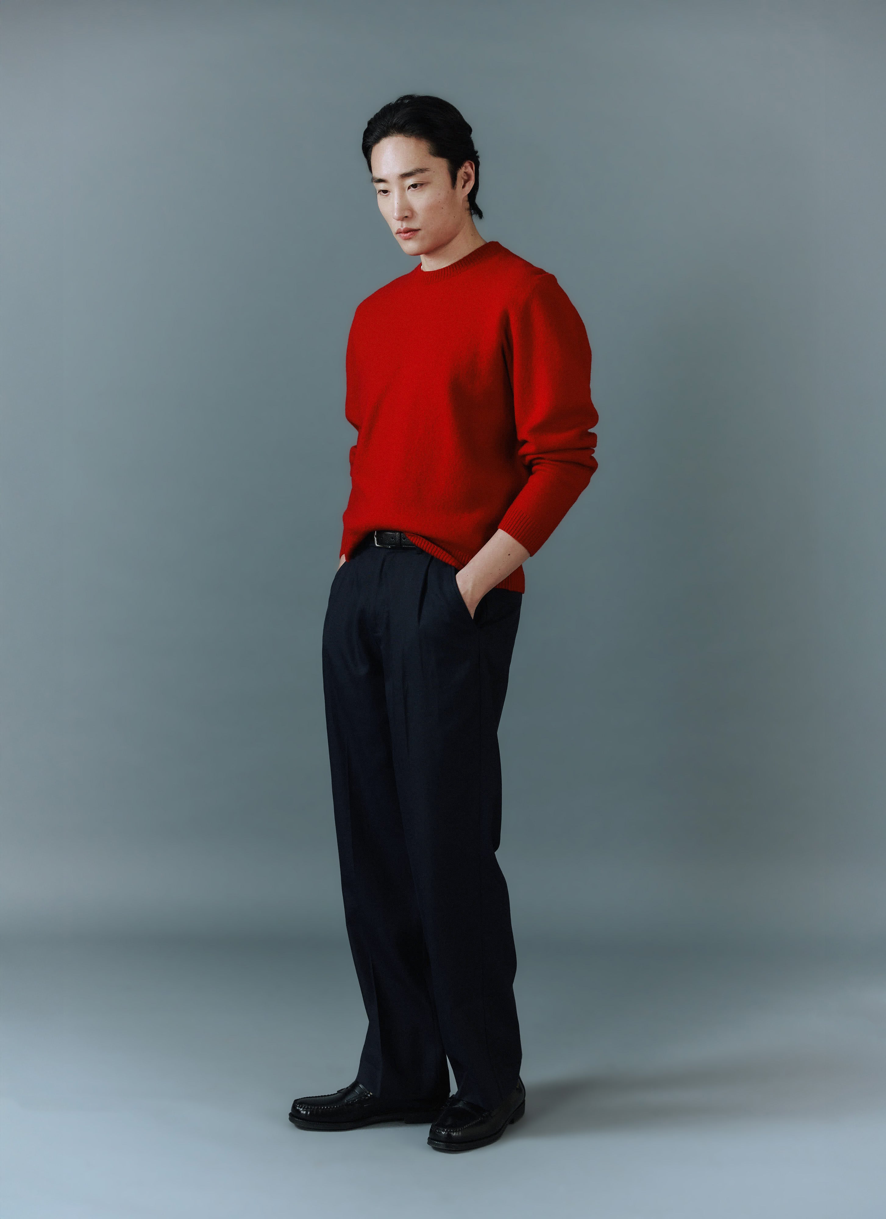 A model wears the red Felted Merino Wool Jumper from Percival with smart black trousers against a grey studio background.
