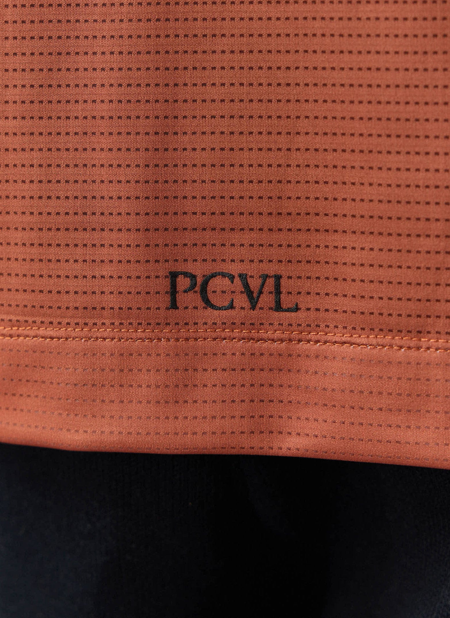 A close-up of the rust-coloured PCVL Performance Top from Percival, showing the breathable fabric and logo detail.