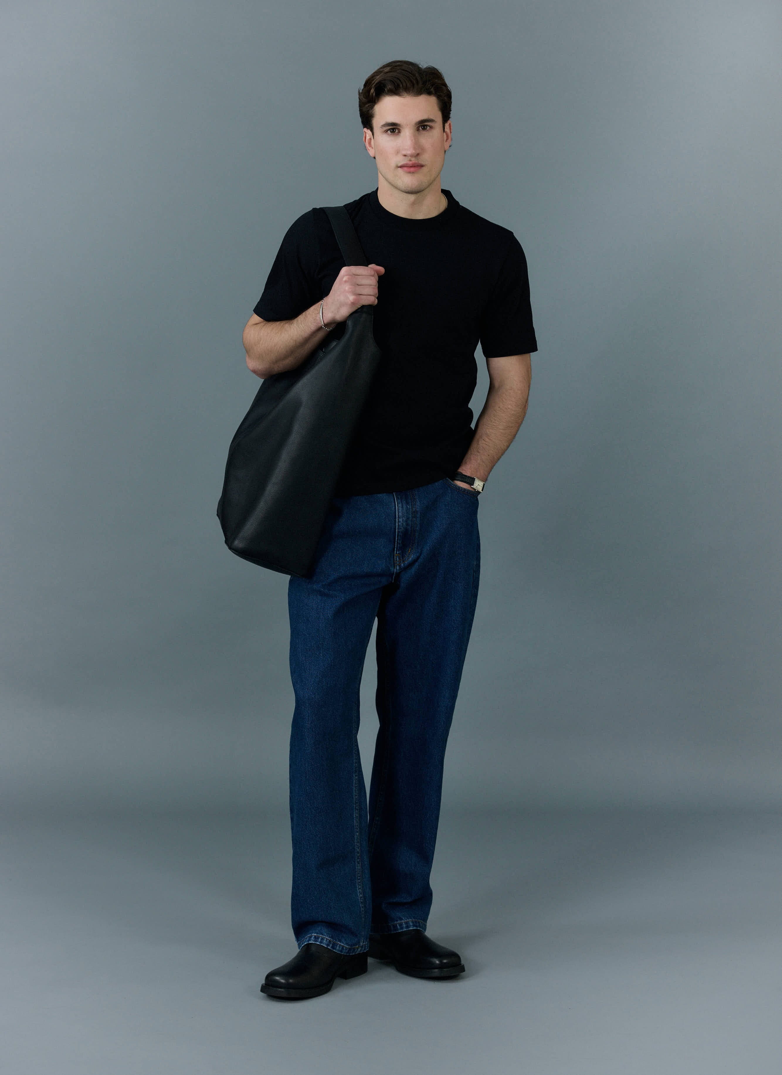 A model wears the Percival Cropped Regular Fit T Shirt in black with dark blue jeans and a large black tote bag.