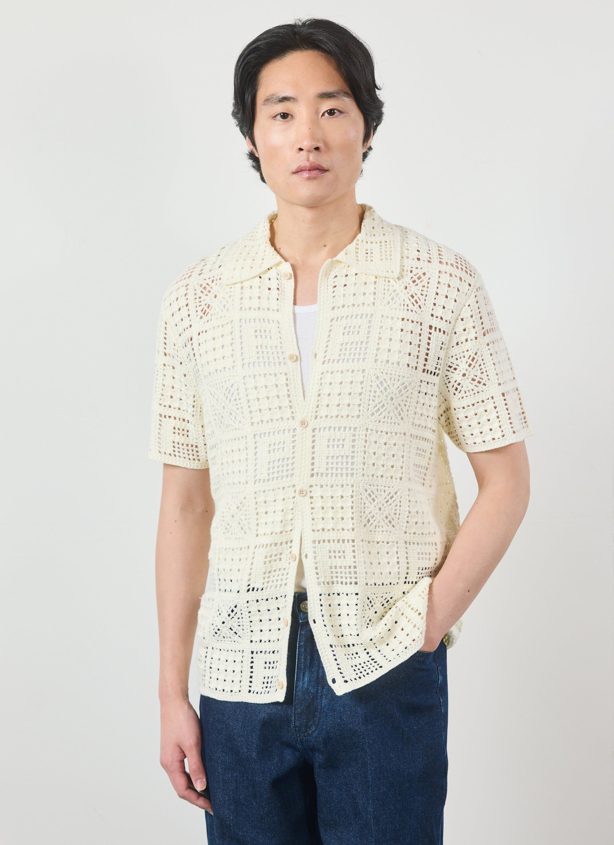 The Percival Crochet Groundsman Shirt in ecru, a short-sleeve cotton knit, shown on a model with a white vest and jeans.