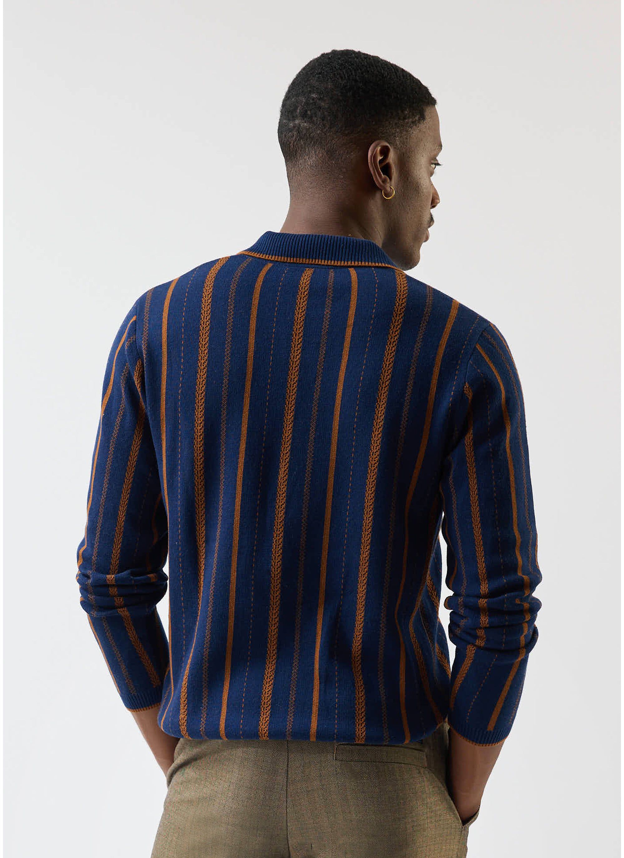A model seen from behind wearing the Percival Citation Knitted Football Shirt in navy with vertical orange stripes.