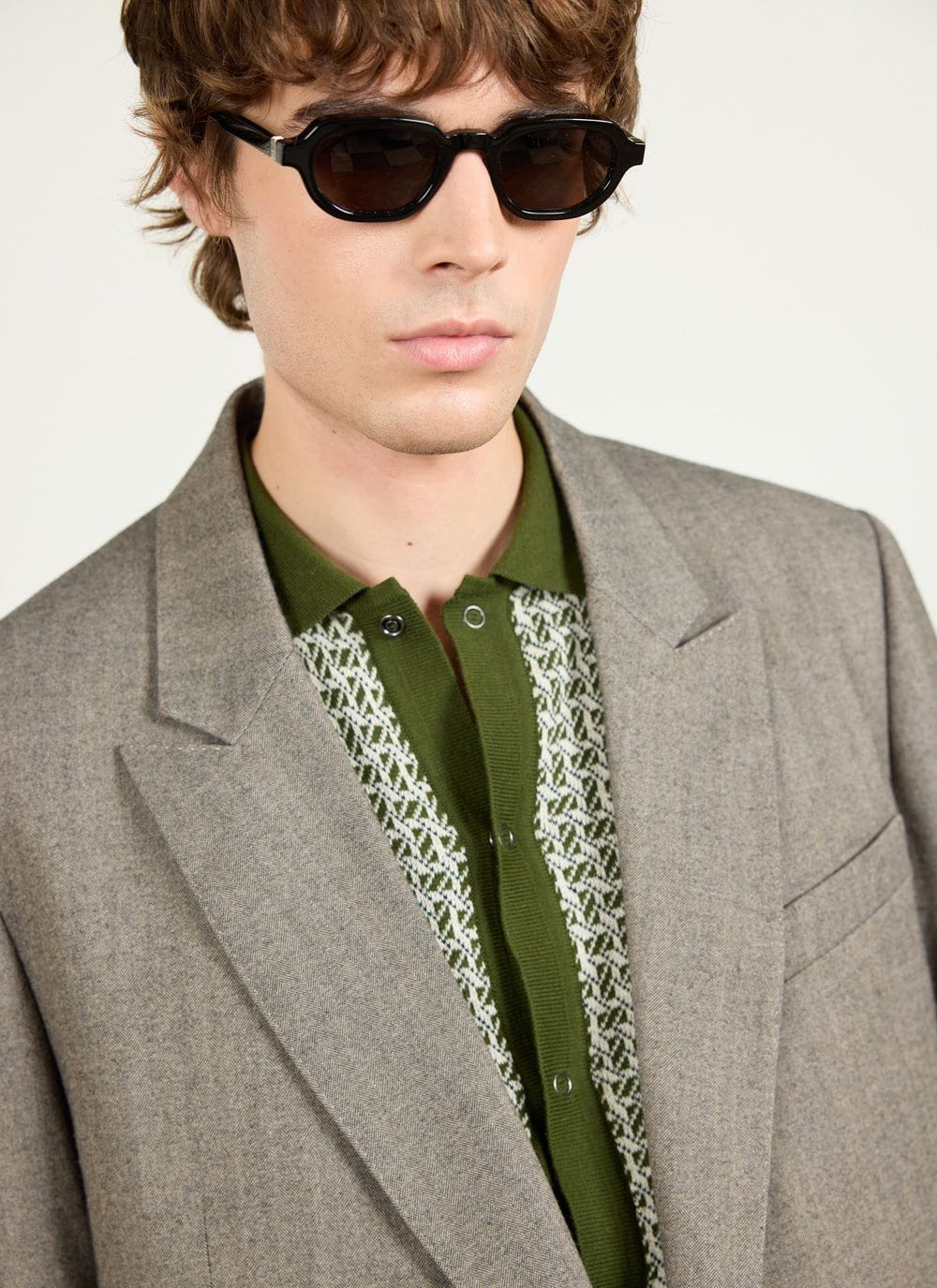 close up of a model wearing the percival grey herringbone double breasted blazer over a green patterned top and sunglasses