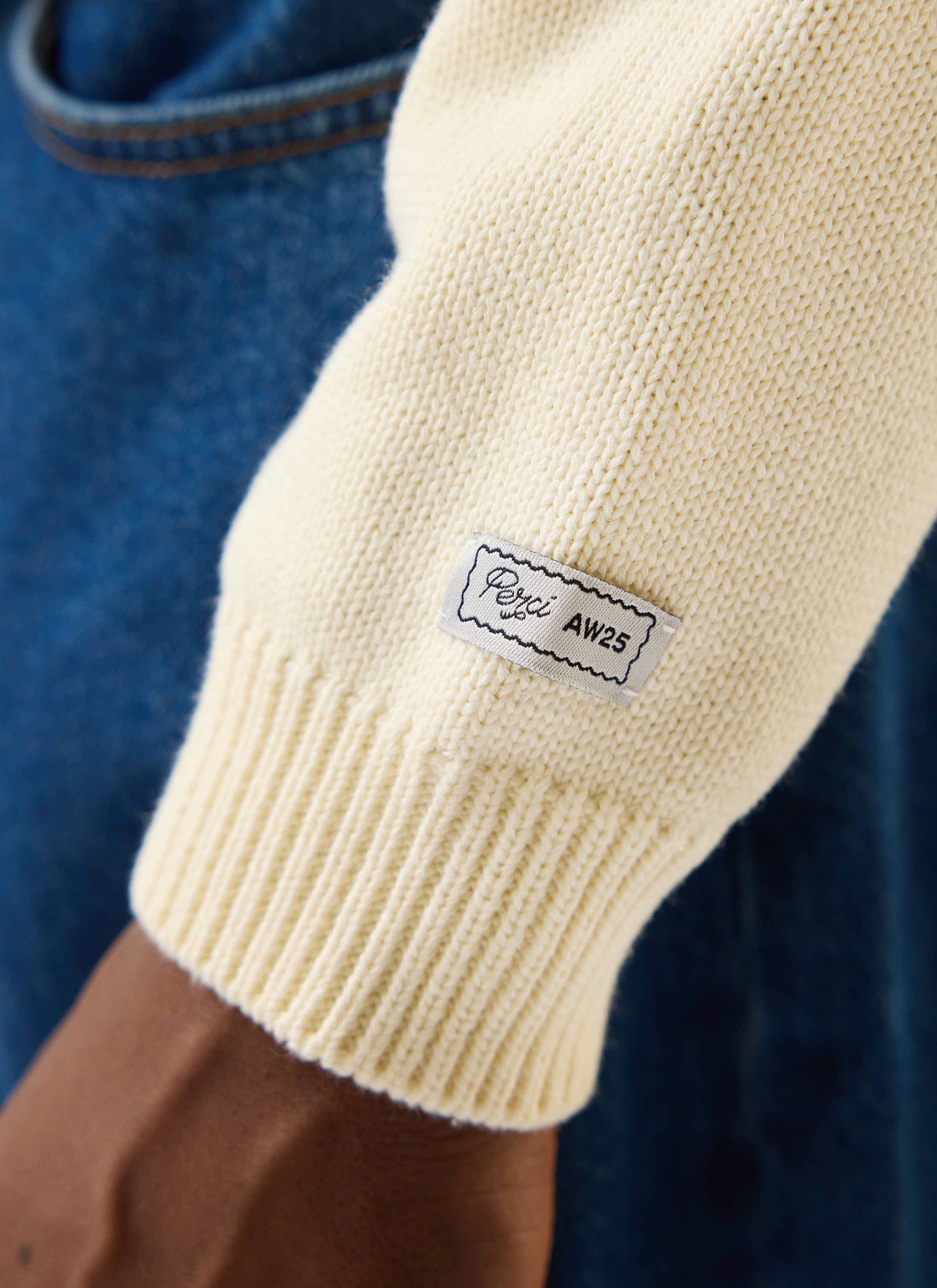 Close-up of the Percival Public Library Knitted Jumper in ecru cream, showing the ribbed cuff detail and branded label.