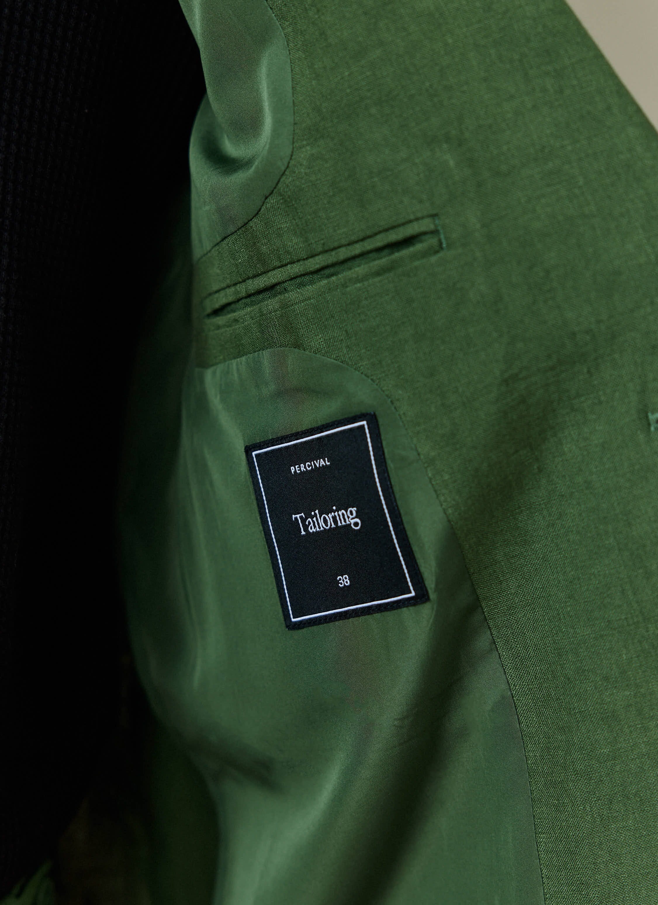 Internal black tailoring label and pocket detail inside the forest green linen blazer by Percival.