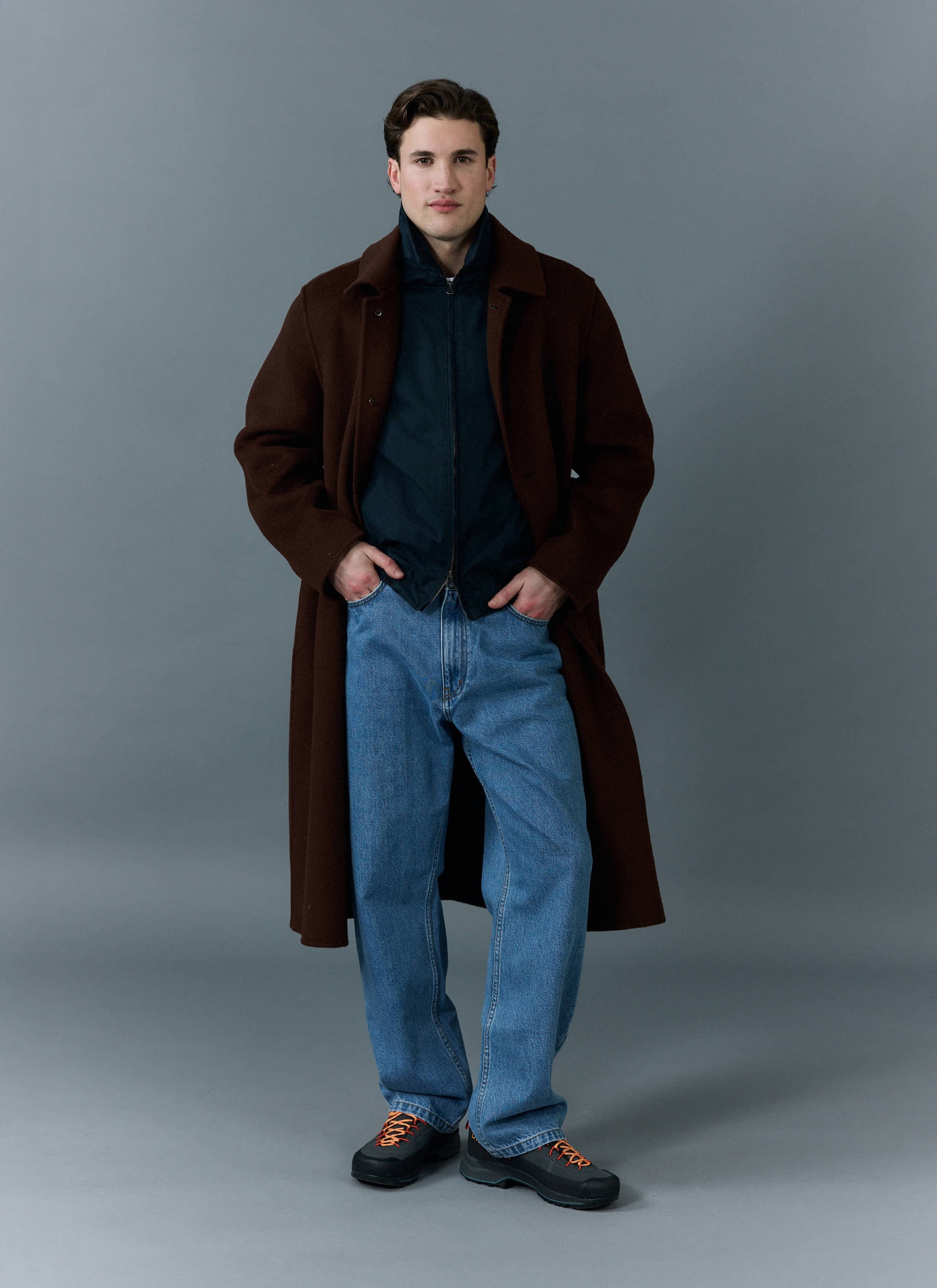 A model wears the Percival Wide Leg Denim Jeans in light wash blue, styled with a brown coat for a layered look.