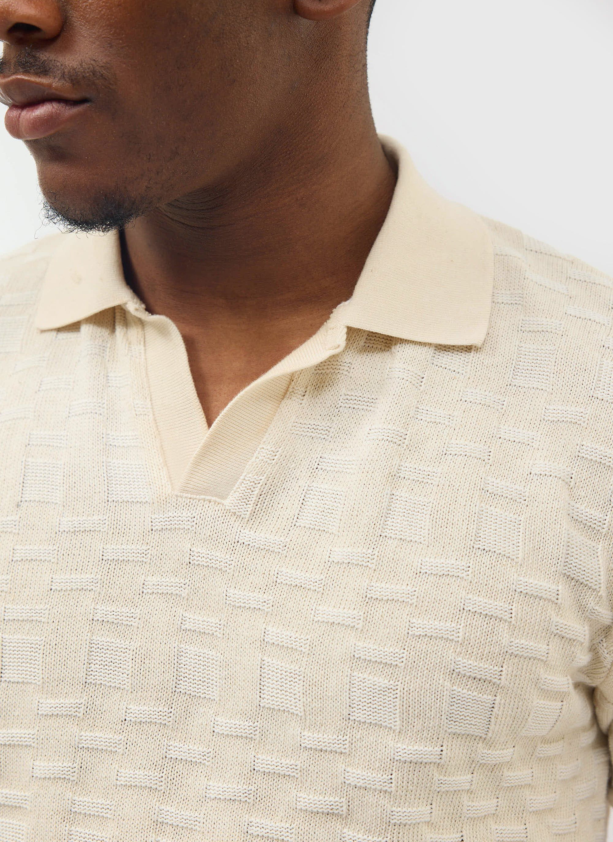 A close-up of a model wearing the ecru Deck Negroni Knitted Shirt from Percival, showing the textured cotton knit and collar.