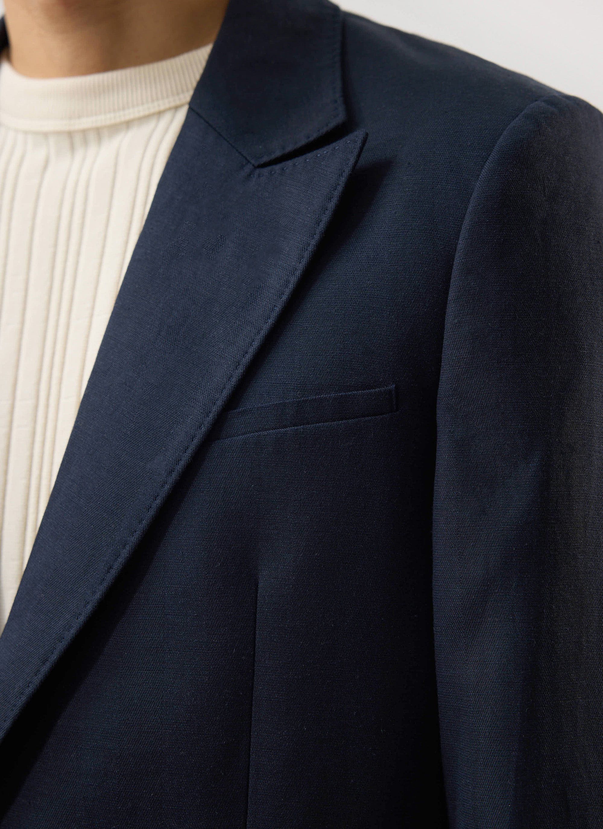 A close-up of a model wearing the navy Percival x Warren Lyocell Tailored Blazer over a cream ribbed jumper.