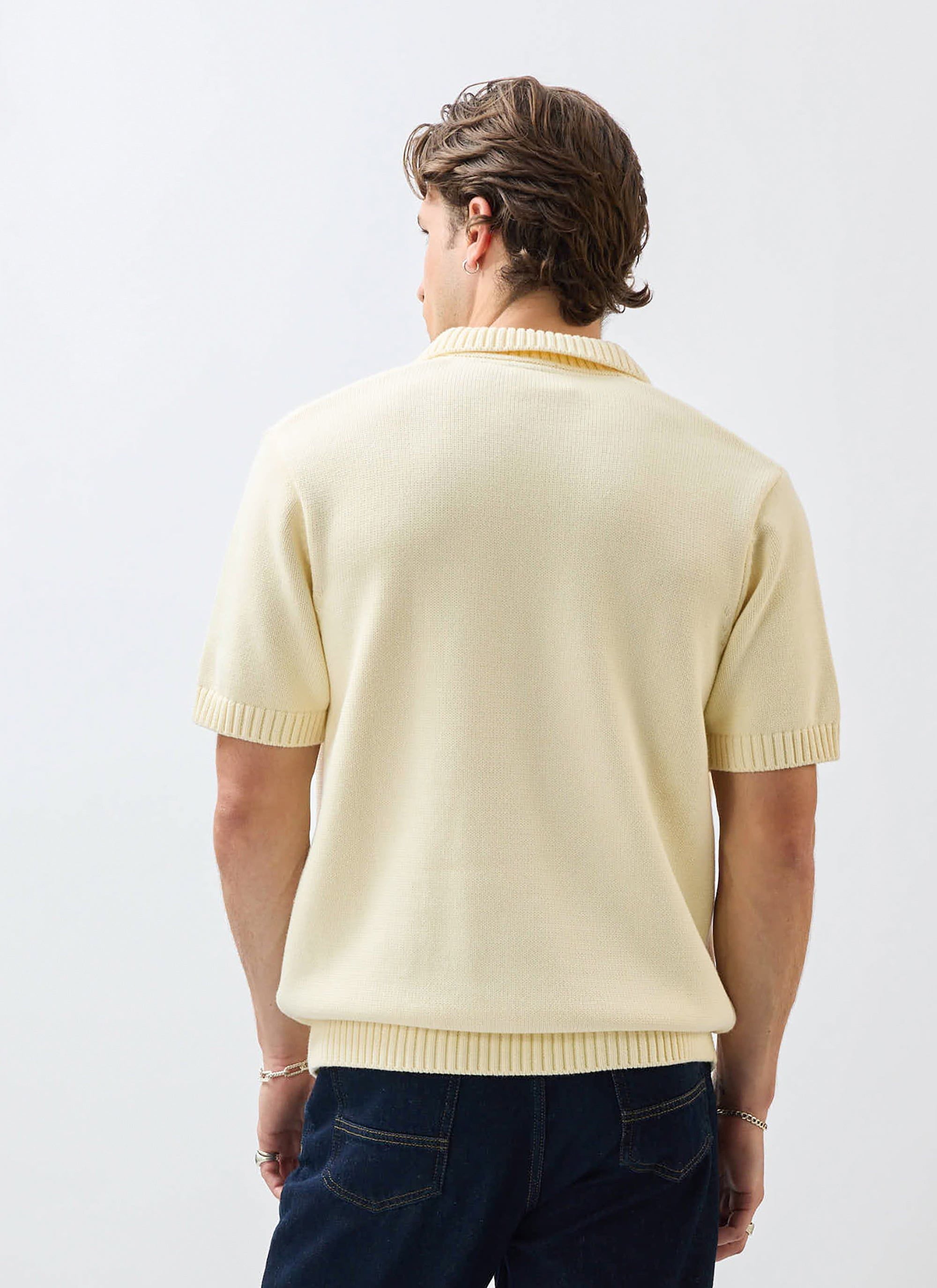 Back view of a model in the Percival Verso Short Sleeve Knitted Shirt in ecru, styled with dark jeans.