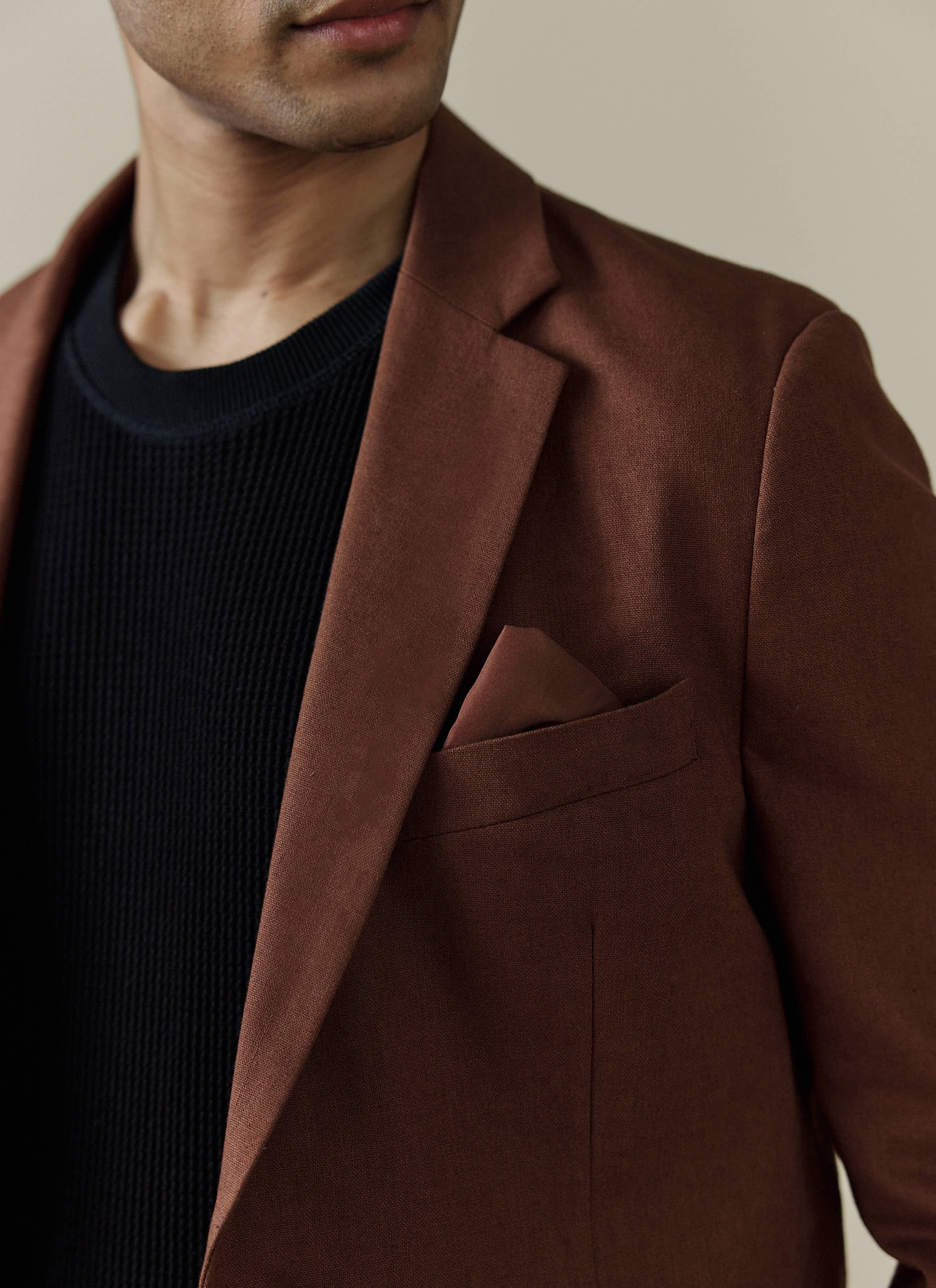 A close-up of a model wearing the brown linen tailored blazer from Percival, showing the lapel and pocket square detail.