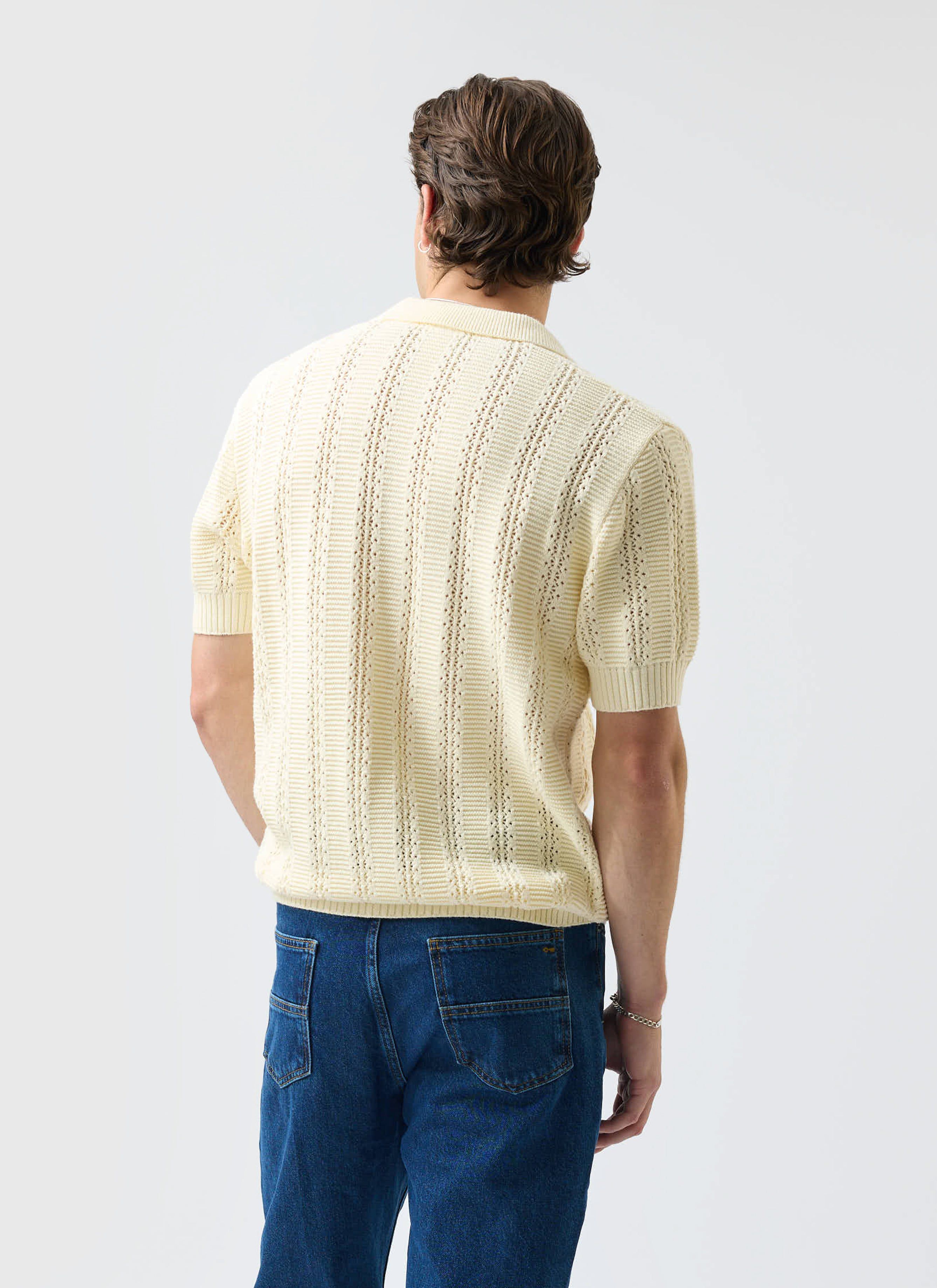 A model from the back wearing the Percival Addendum Knitted Polo Shirt in ecru cream with blue jeans.