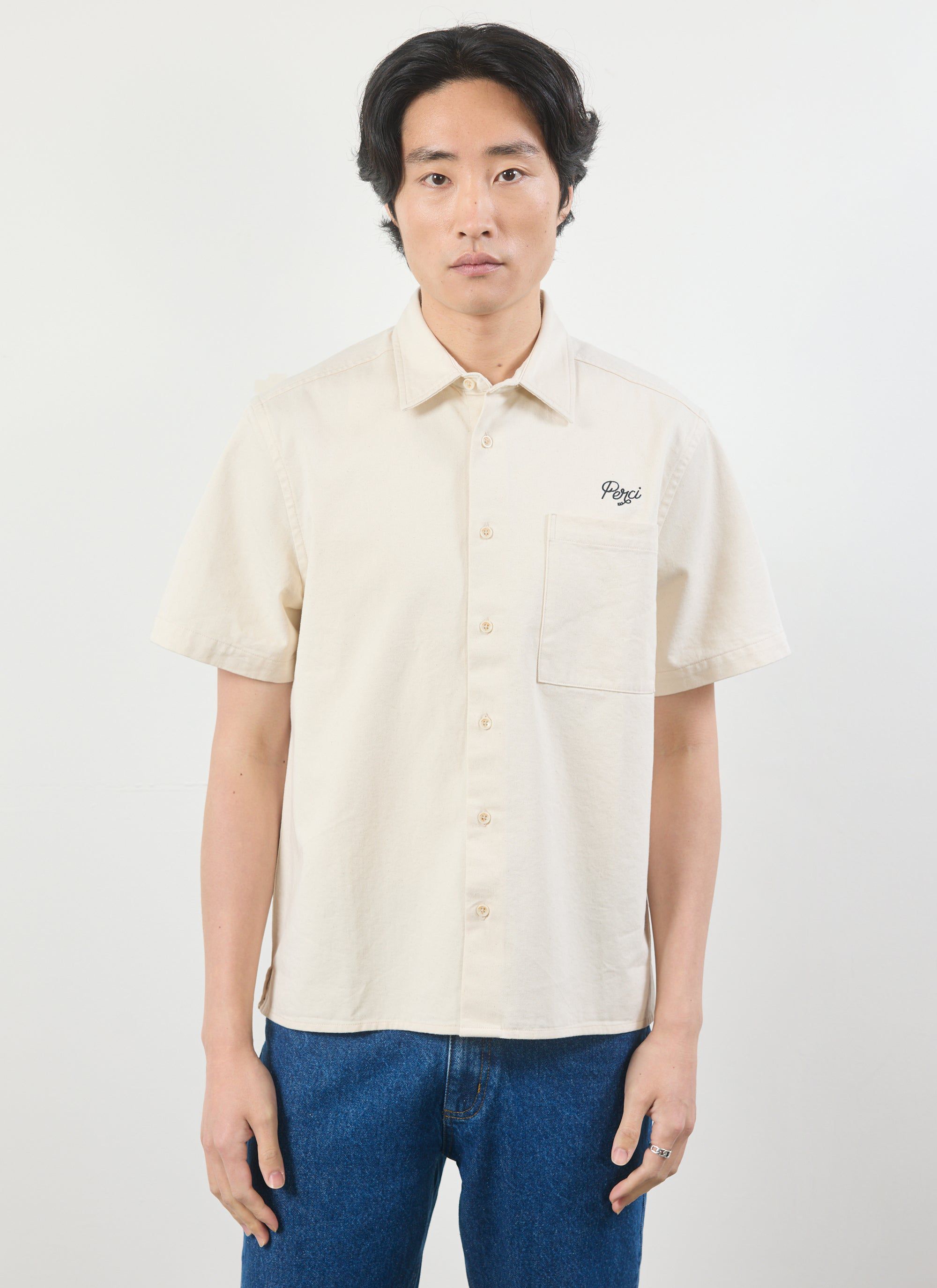 A model wears the Percival Olive Embroidered Cropped Shirt in off-white, showing the front view with Perci chest embroidery.