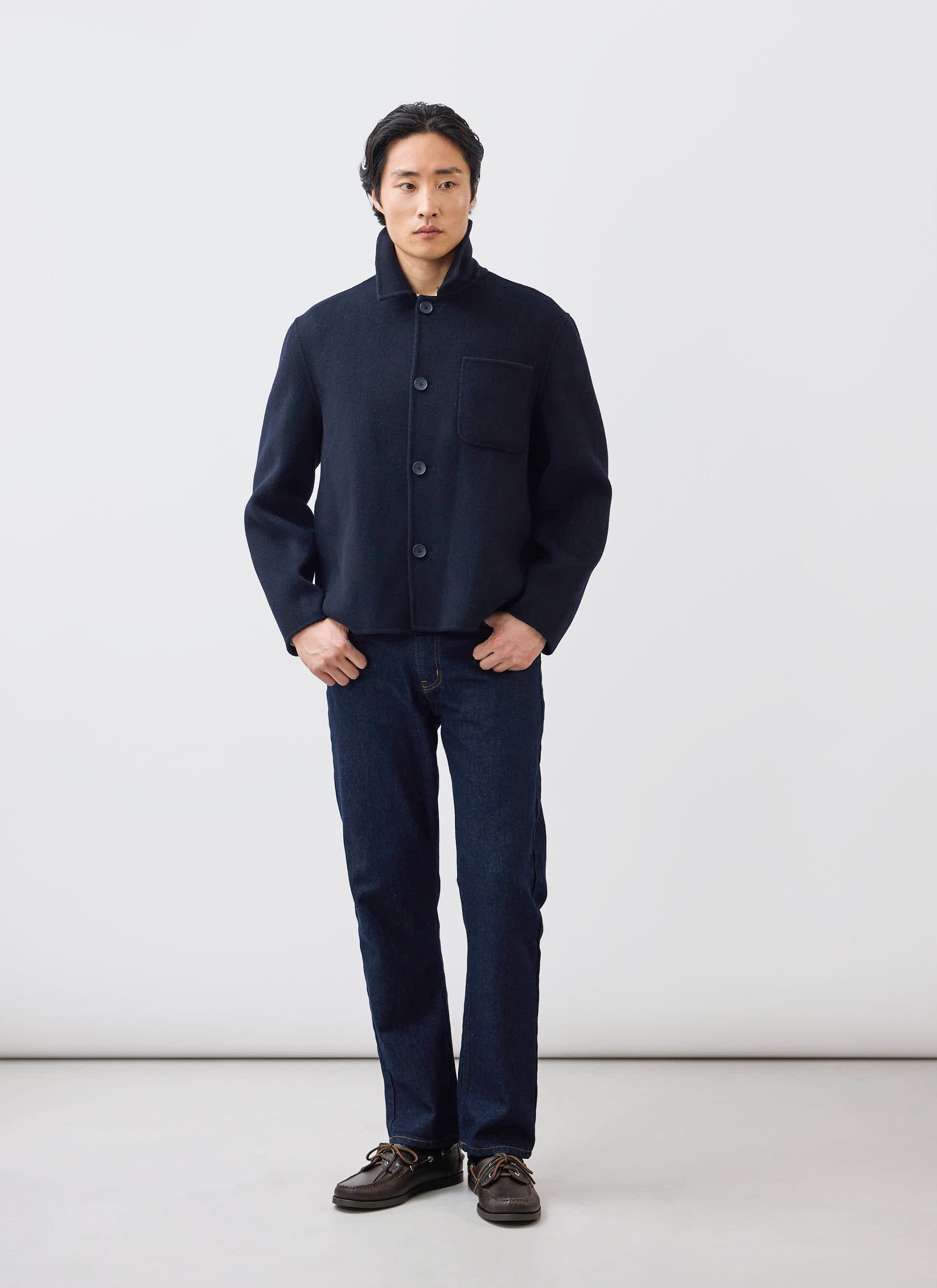 A man models the Percival Heavy Wool Overshirt in navy, paired with dark jeans and boat shoes in a studio.