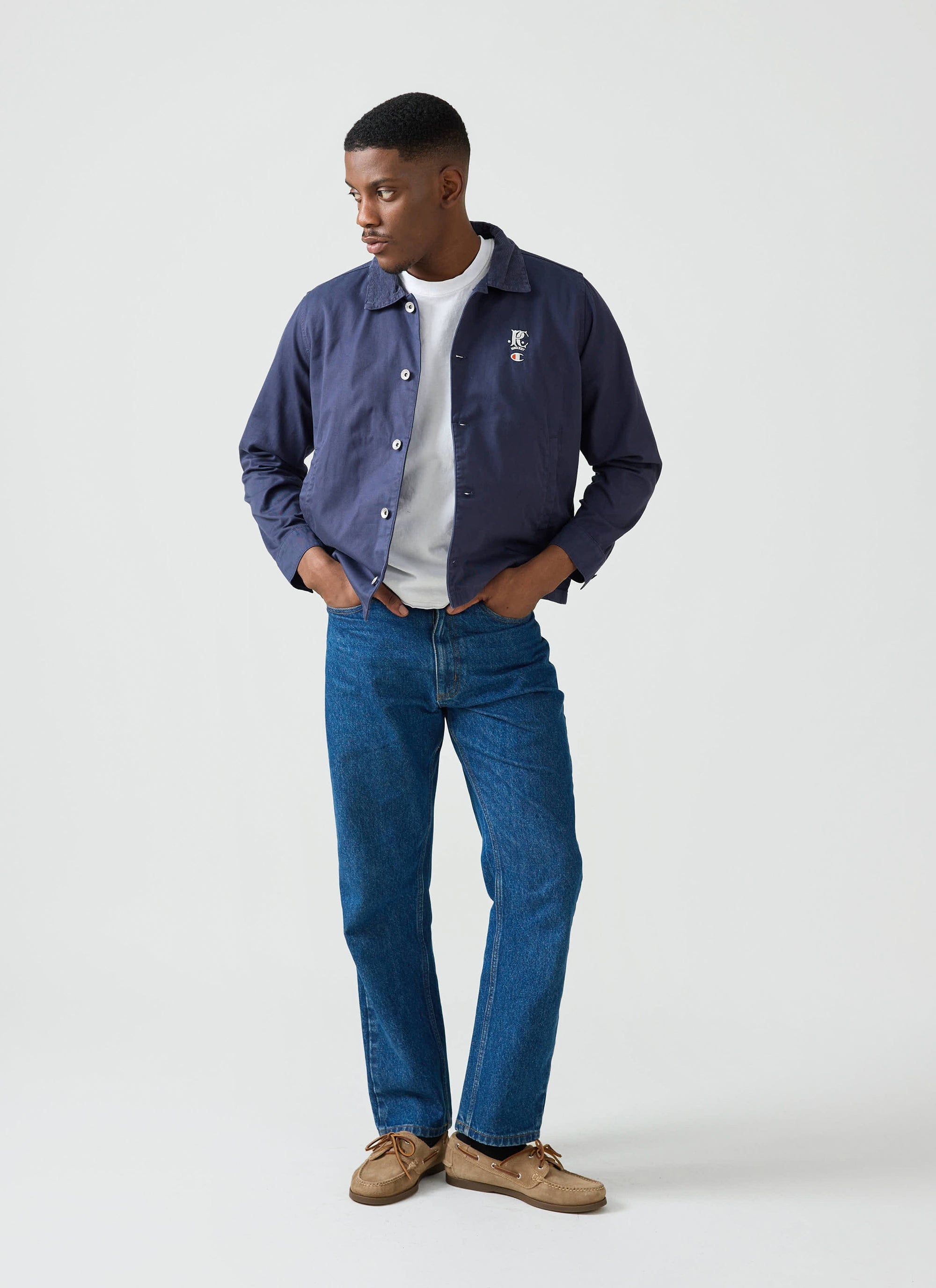 A model wears the navy Cord Collar Jacket from the Champion x Percival collection, styled with a white tee and blue jeans.