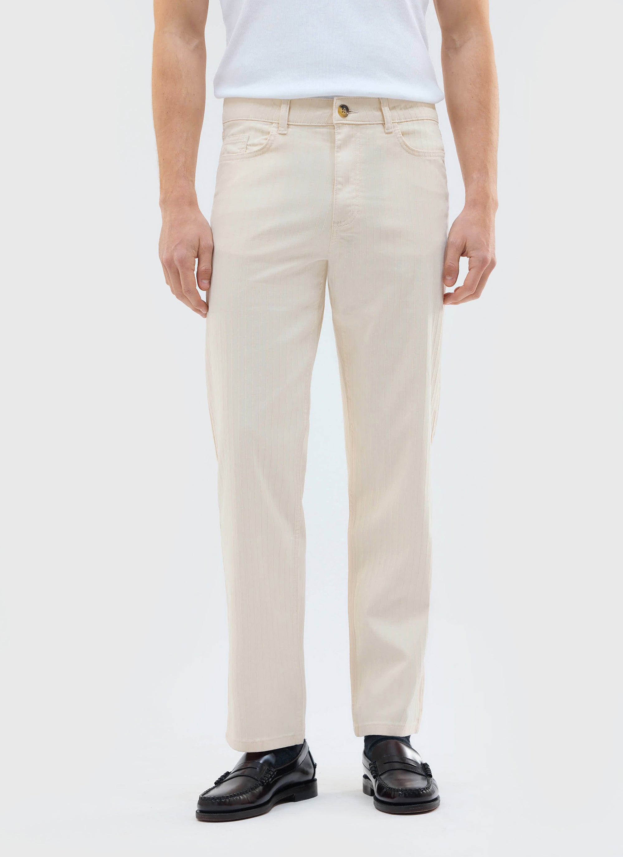 A model wears the Percival Rocco 5 Pocket Trousers in ecru, styled with a white vest and black loafers.