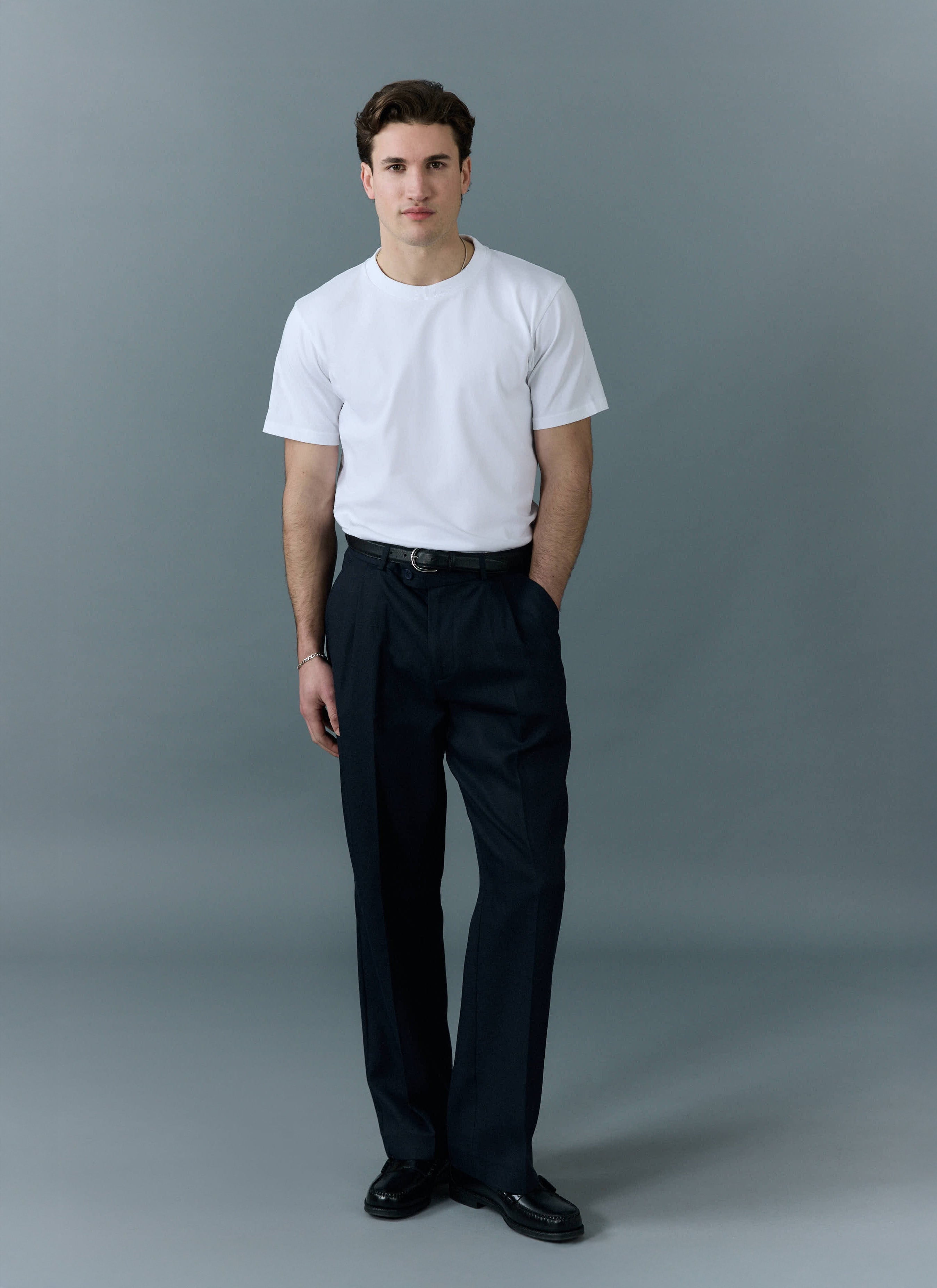 a model wears a percival plain white t shirt with dark trousers and loafers