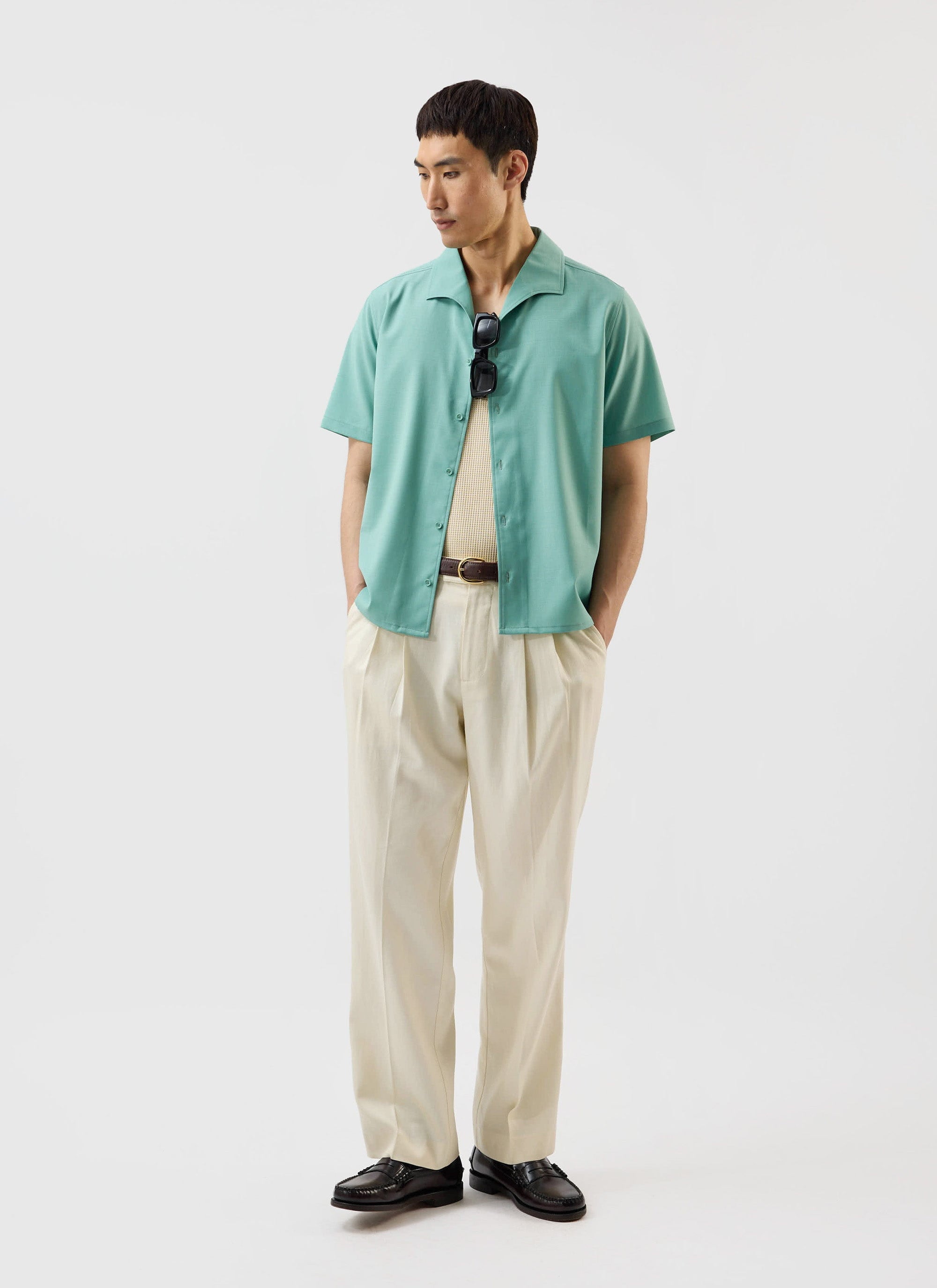 A model wears the Percival x Warren Drape Cuban Shirt in mint green, open over a vest with cream pleated trousers.