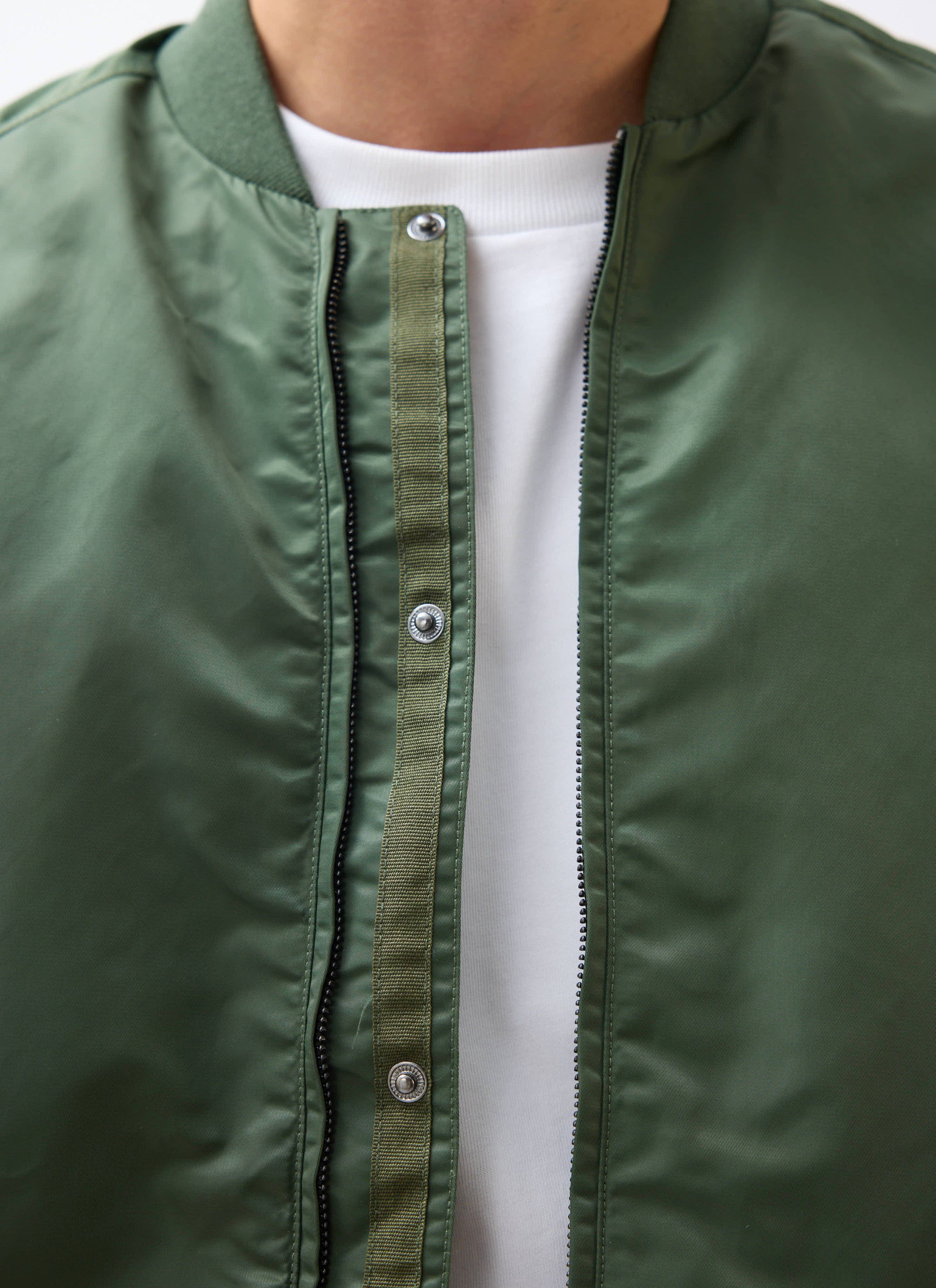 A close-up of the Percival Nylon Bomber Jacket in forest green, showing the zip and button placket detail.