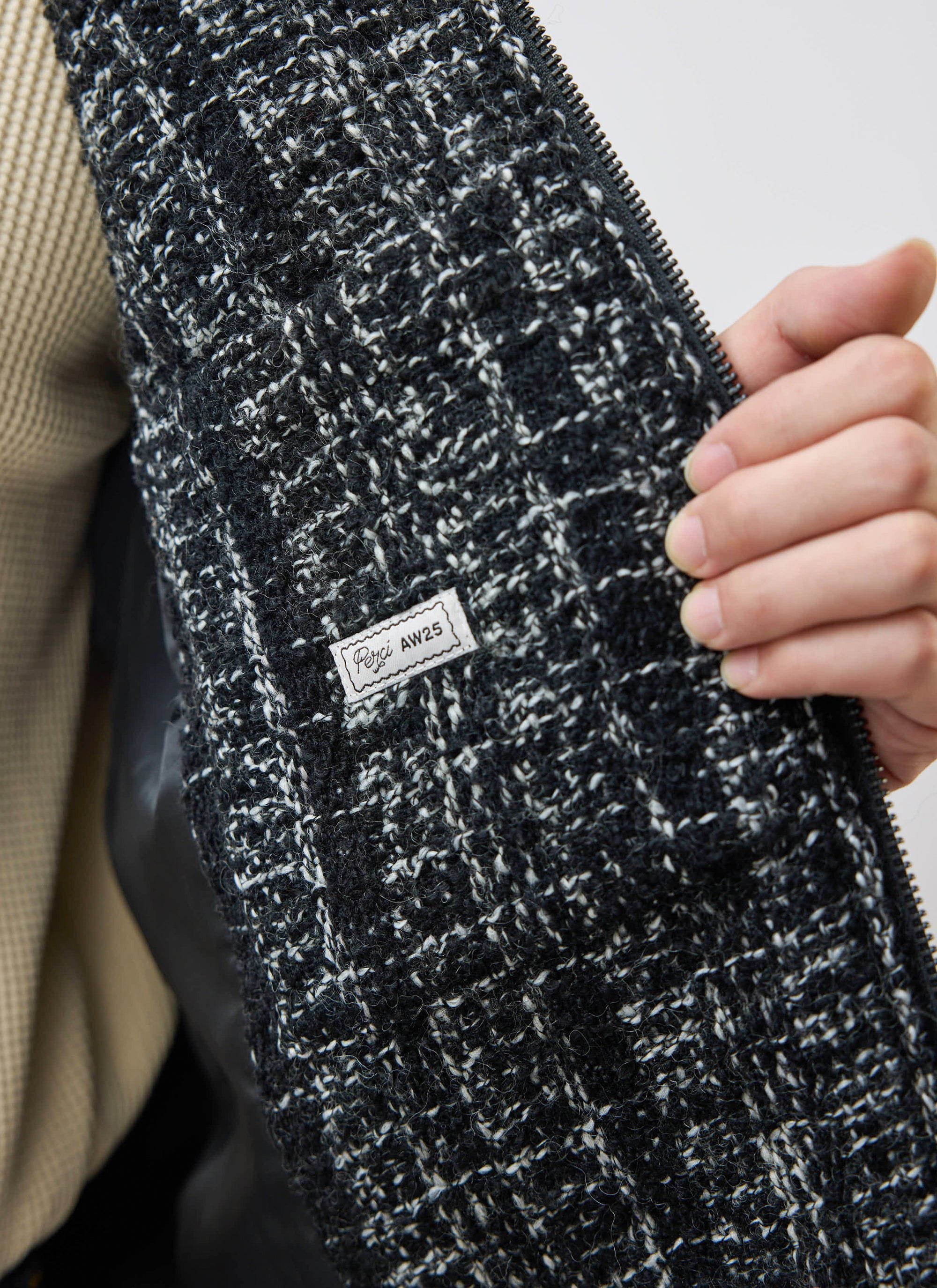 Close-up of the Percival Ingegno Zip Jacket in black, highlighting the bouclé tweed texture and internal AW25 label.