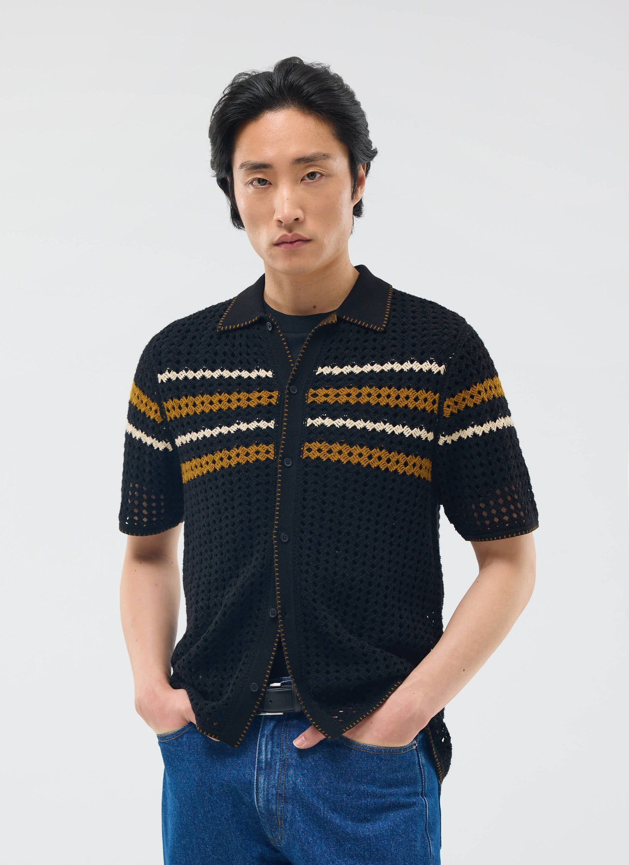 A model wears the Percival Pesaro Knitted Shirt in black, a crochet-style top with gold and white stripes across the chest.