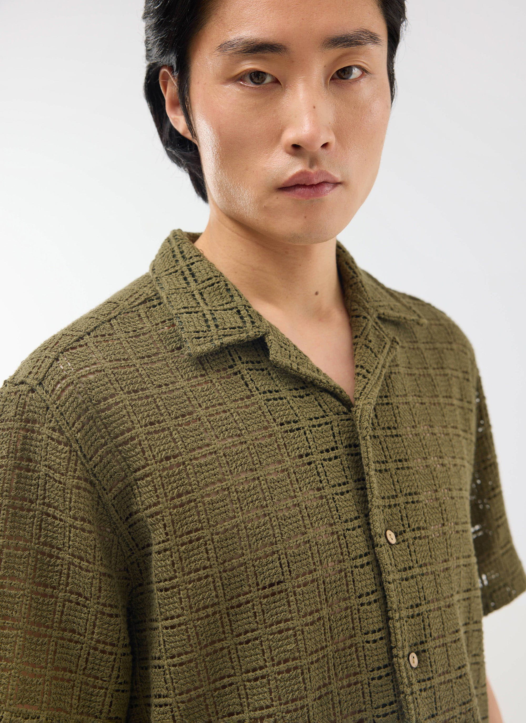 A studio close-up of a model wearing the Percival Palermo Crochet Cuban Shirt in olive green, showing the intricate fabric.