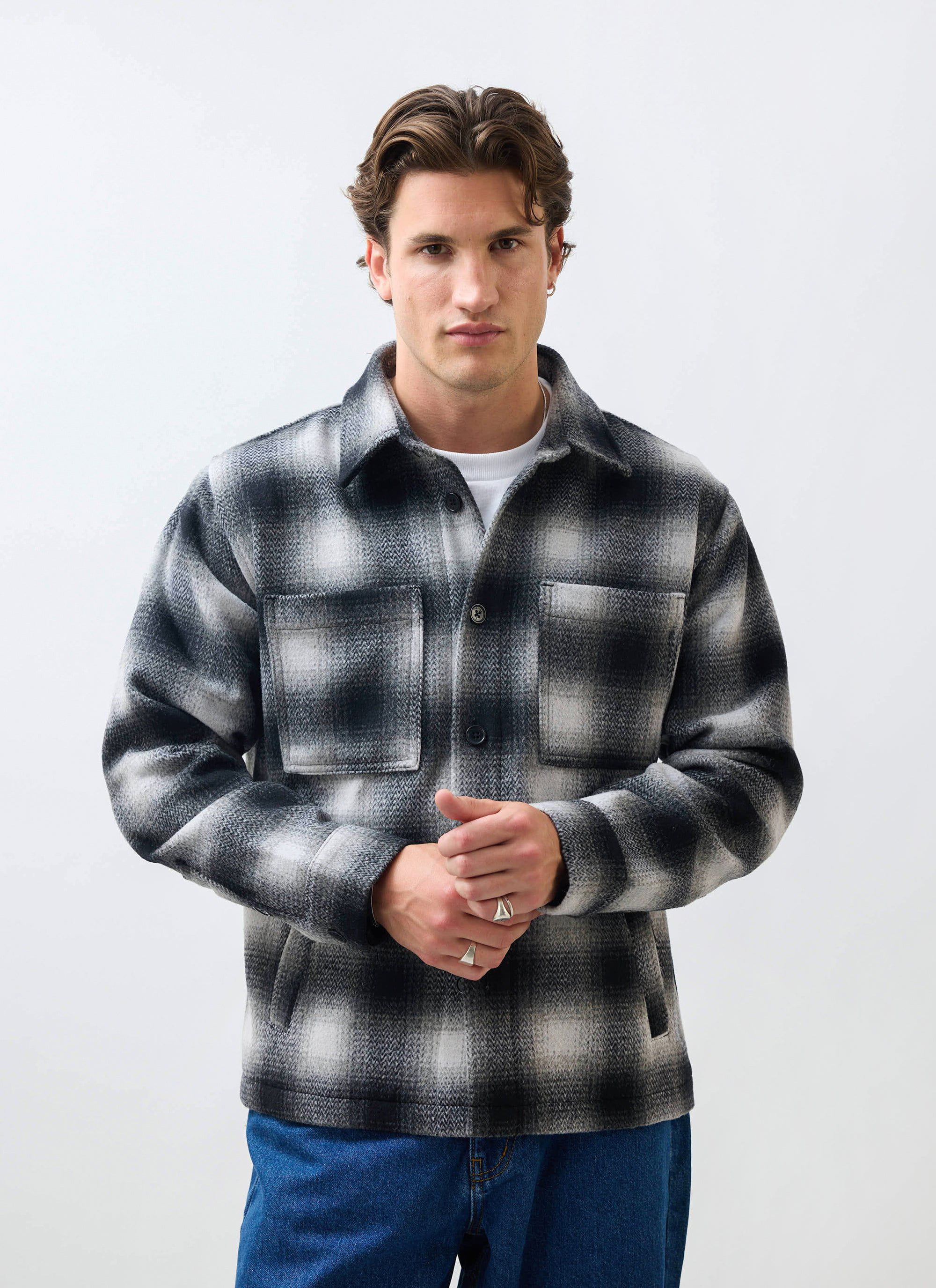 A male model wears the Percival Check Overshirt in a grey and black wool blend against a white studio background.