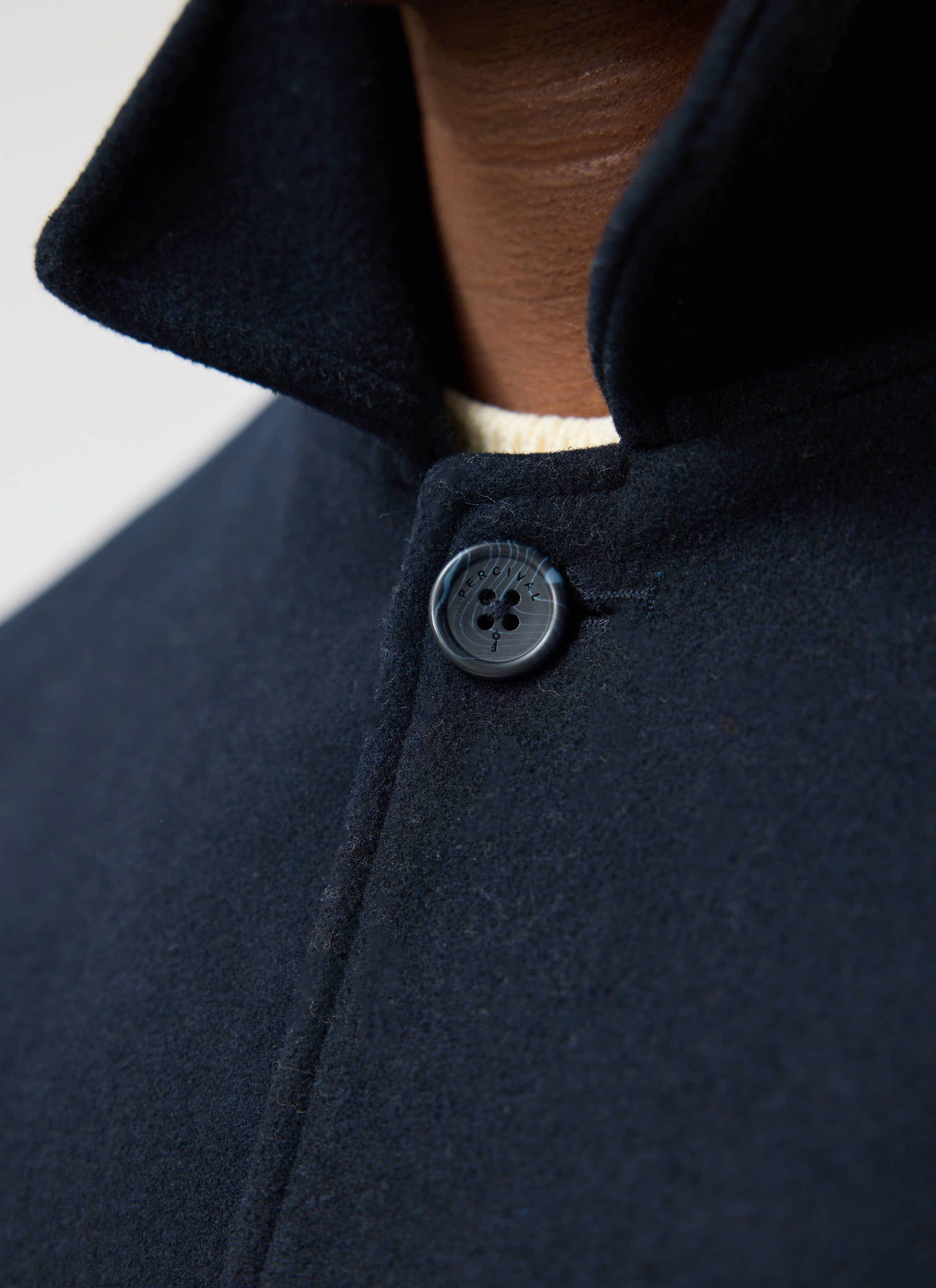 A close-up of the Percival navy peacoat in Melton wool, showing the detailed branded button and collar.