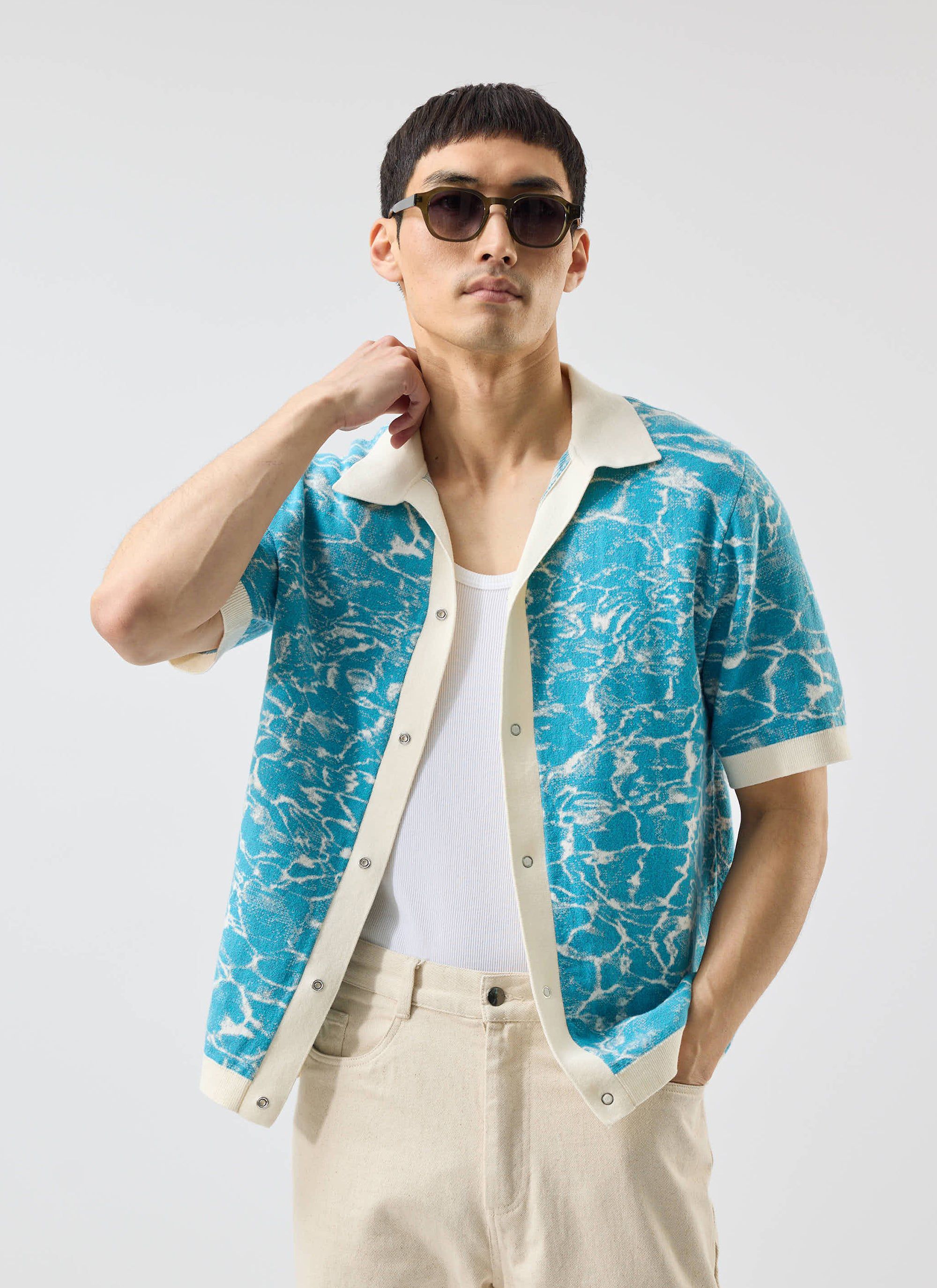 A model wears the Percival Farraris Negroni Knitted Shirt in blue and white, styled open over a vest with sunglasses.