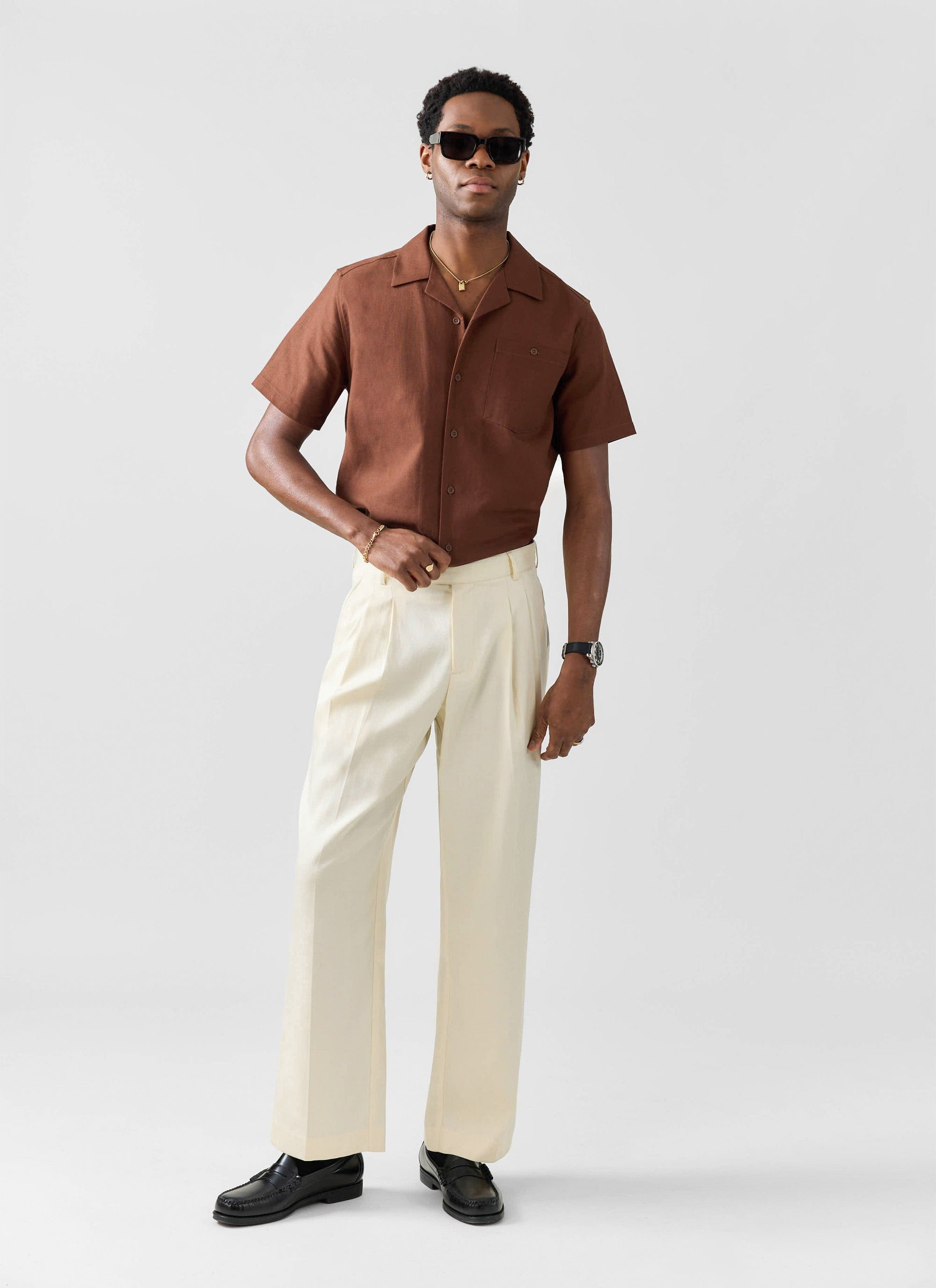 A model wears the brown linen Percival Cuban shirt, styled with cream trousers, black loafers, and sunglasses.