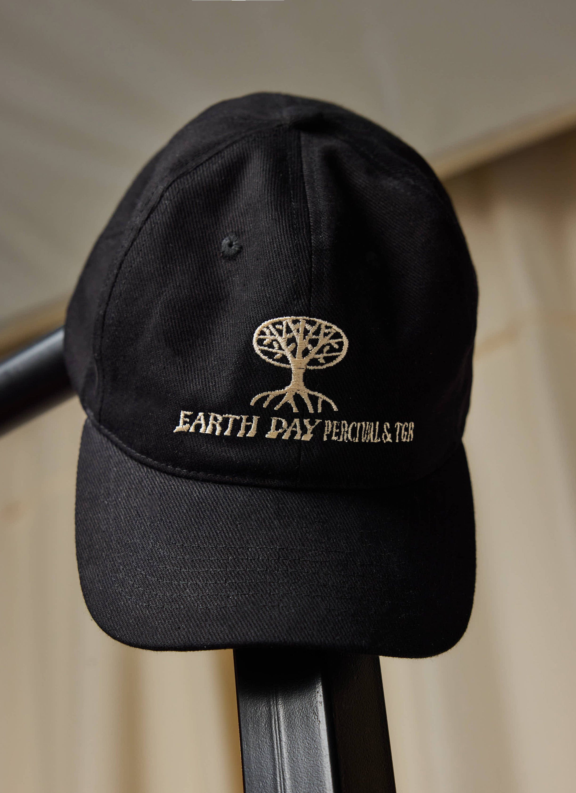 The Percival x The Gorilla Brand black cotton cap, featuring Earth Day embroidery, resting on a black rail.