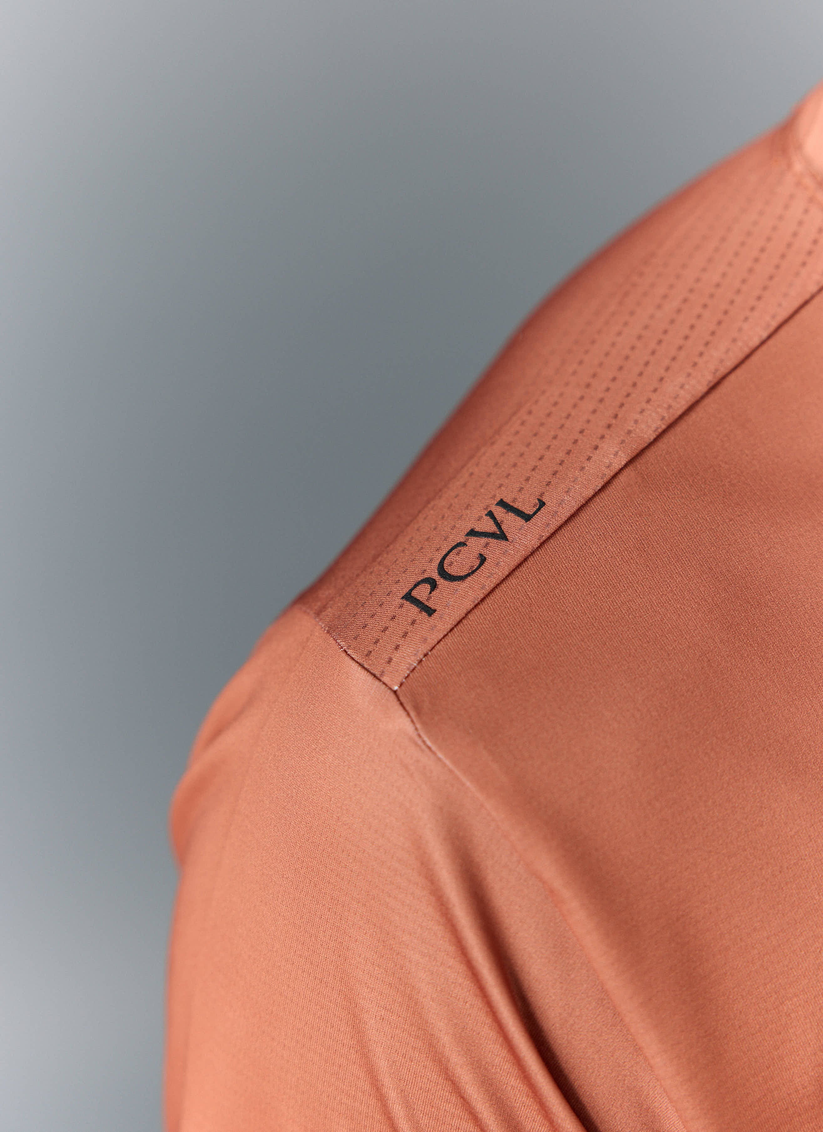 A detailed close-up of the Percival PCVL Performance Top in rust, showing the black logo and perforated shoulder detail.