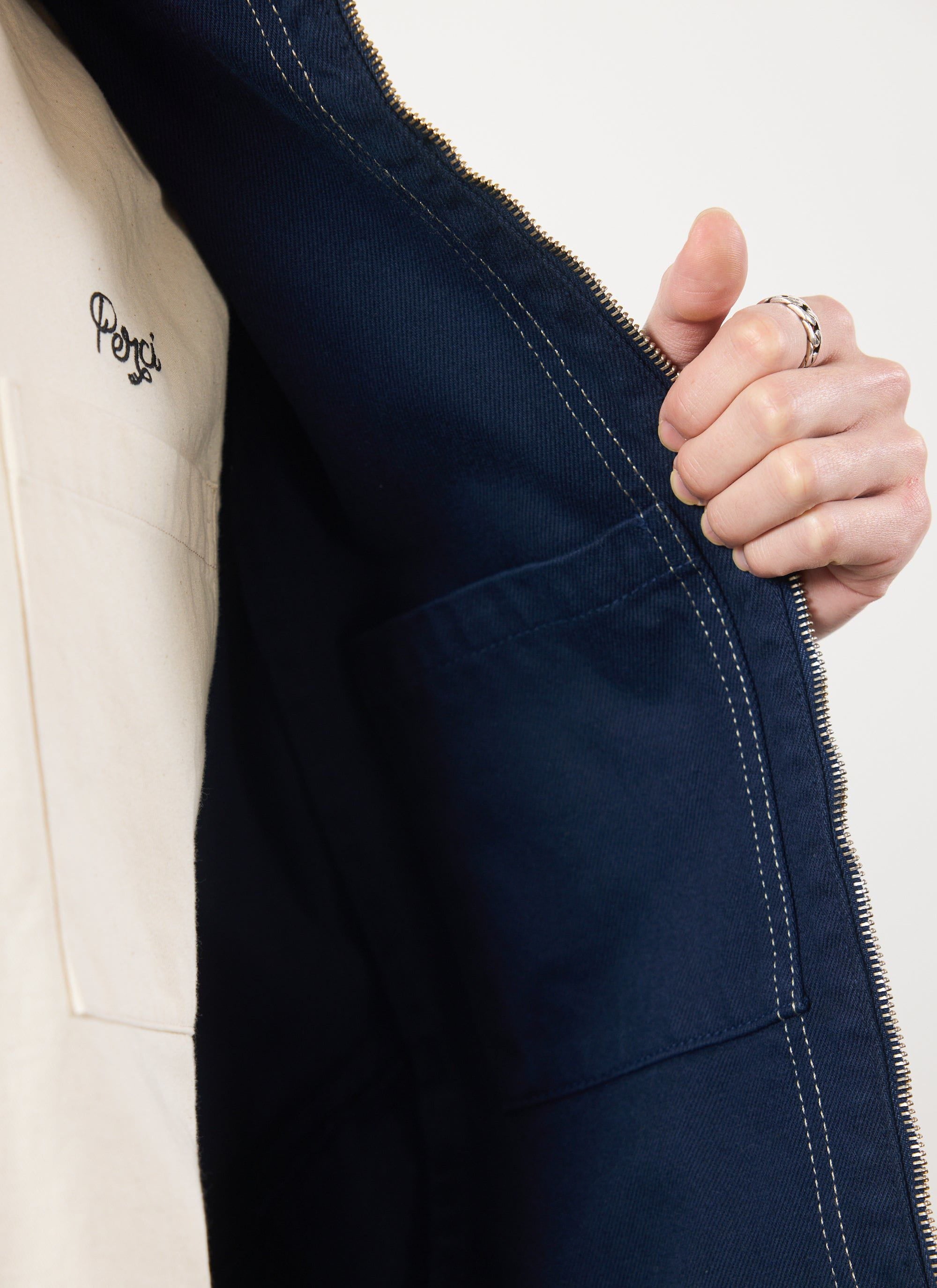 A close-up of the inside of the navy Percival Calabria Harrington jacket, showing the internal pocket and contrast stitching.