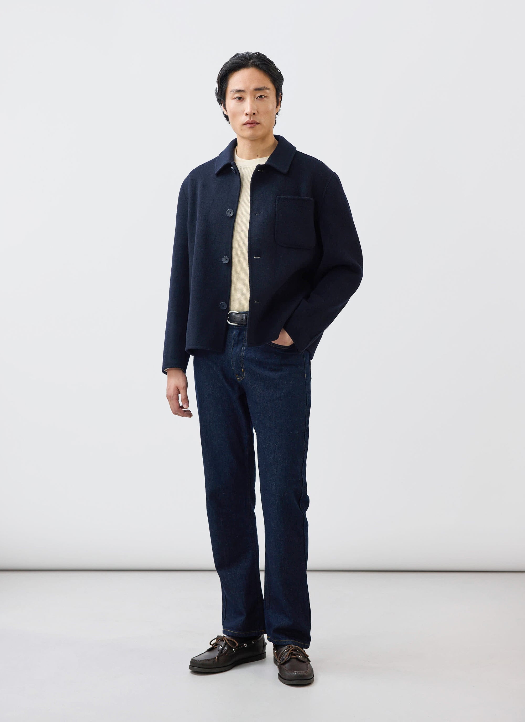 A model styles the Percival Heavy Wool Overshirt in navy, worn open over a cream knit jumper and dark blue jeans.