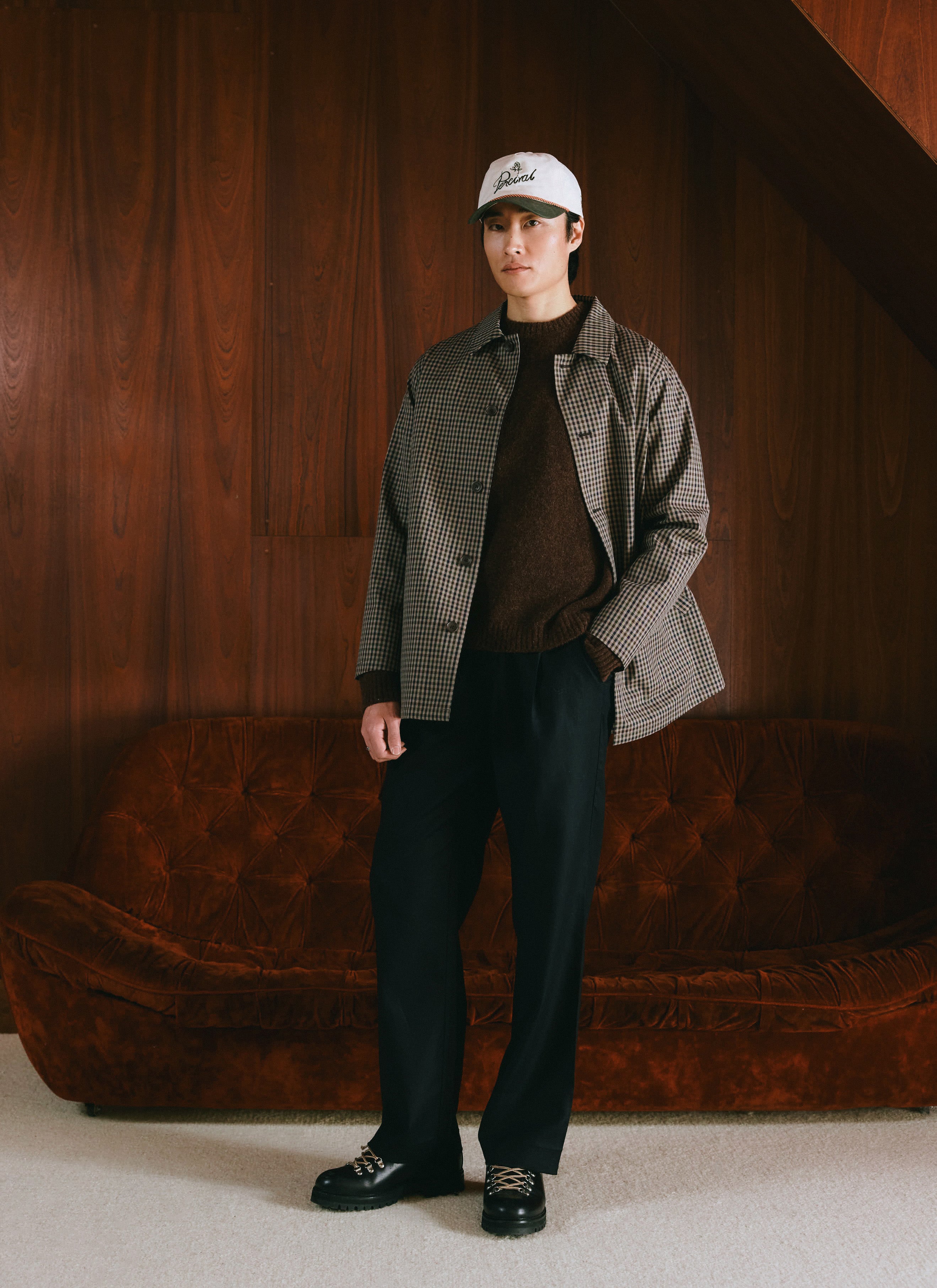 A model wearing the Percival Sherlock short trench coat in Watcher Check over a brown sweater and dark trousers.