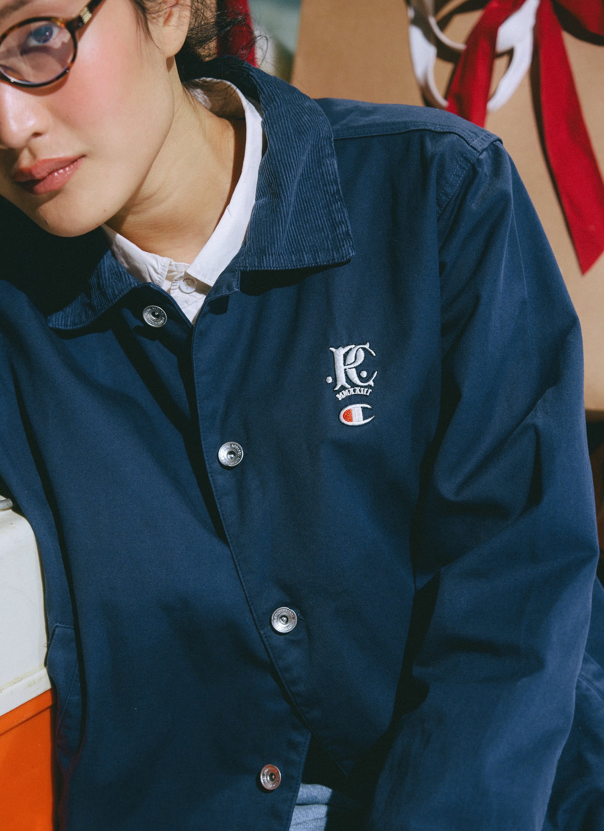 A close-up of a model wearing the navy Champion x Percival Cord Collar Jacket, focusing on the chest embroidery.