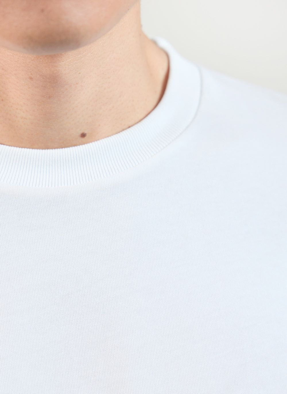 A close up detail shot of the ribbed neckline on a Percival men's white oversized organic cotton t-shirt.