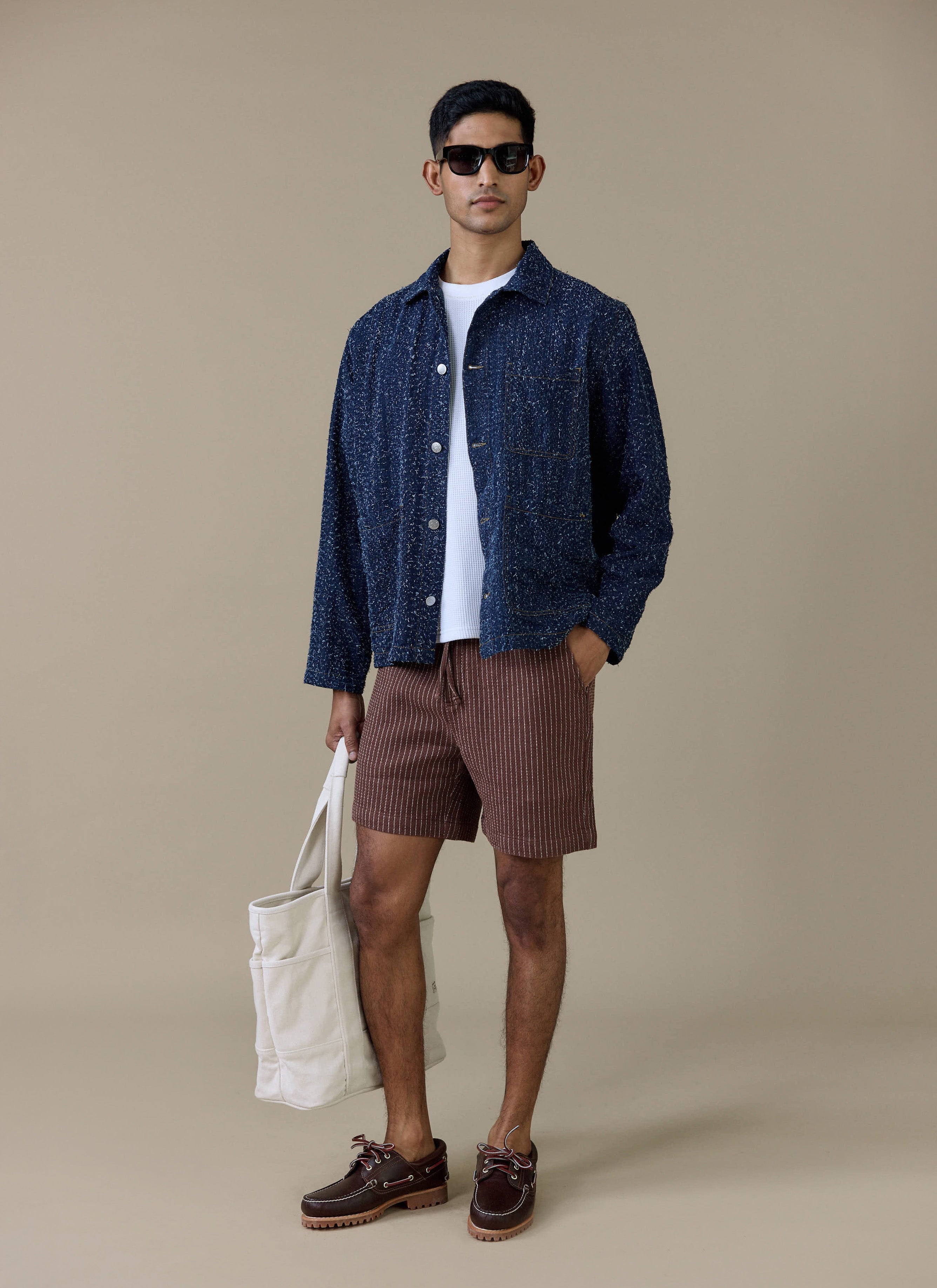 Model wearing the brown linen Sorrento Shorts by Percival with a subtle vertical stripe and a blue overshirt.