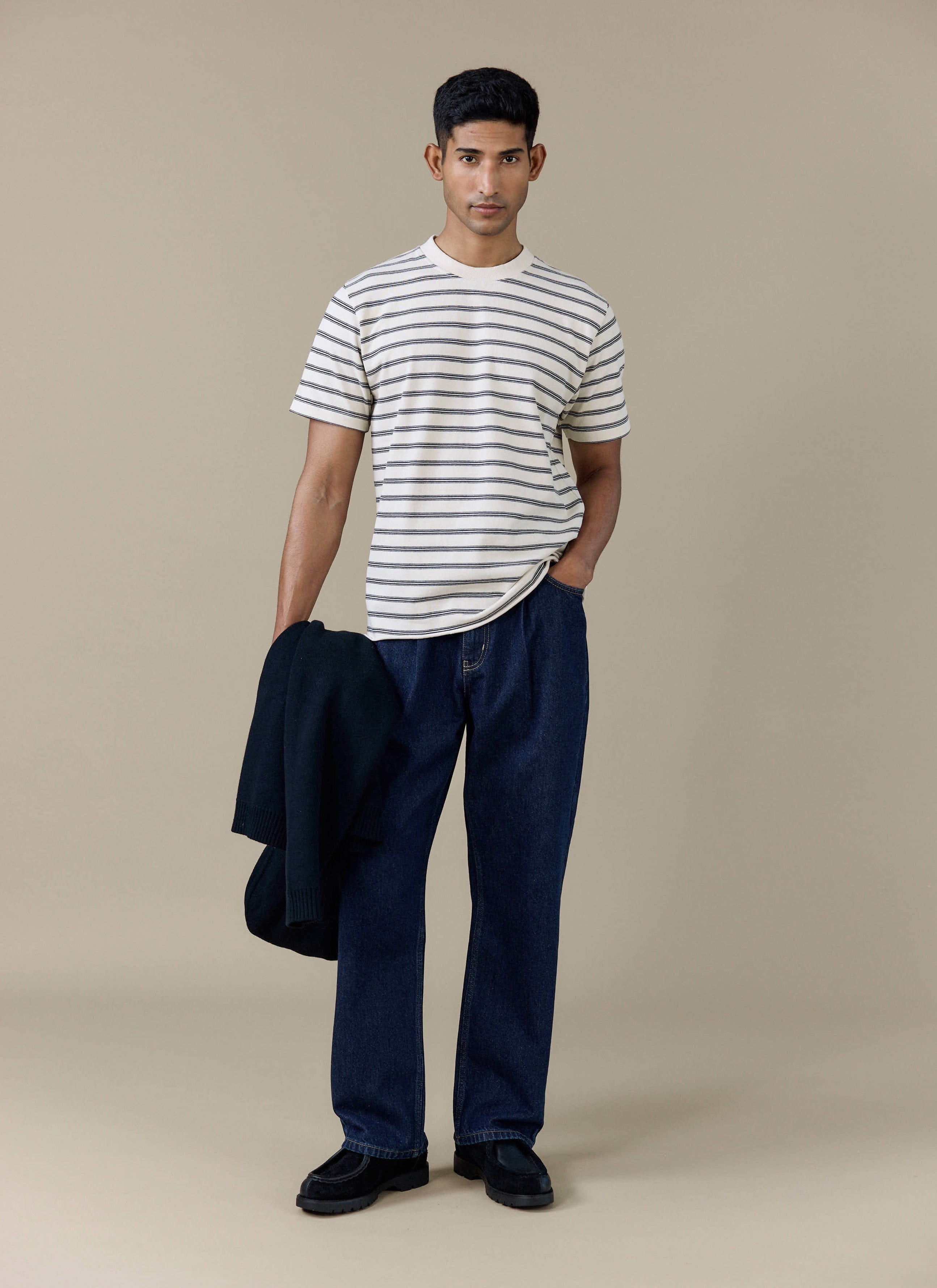 A model wearing the Percival Arlo Raw Hem Breton T Shirt in white stripe organic cotton, styled with dark denim jeans.