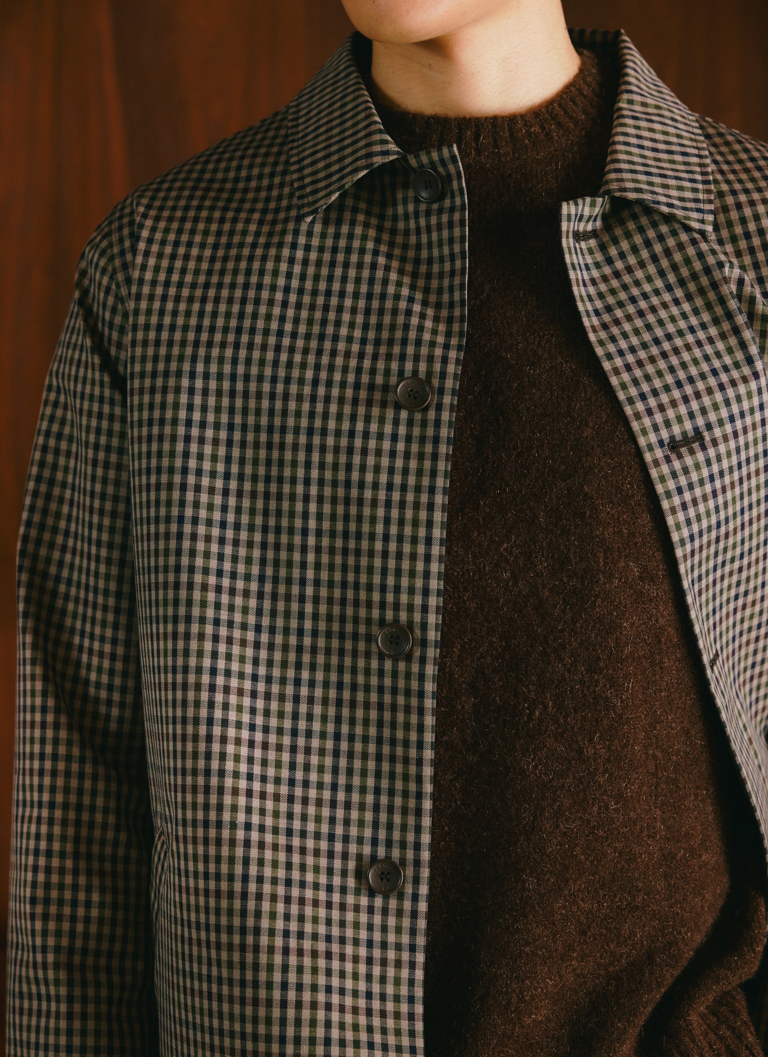 Close-up of a Percival waterproof short trench coat in Watcher Check worn over a brown knit jumper.