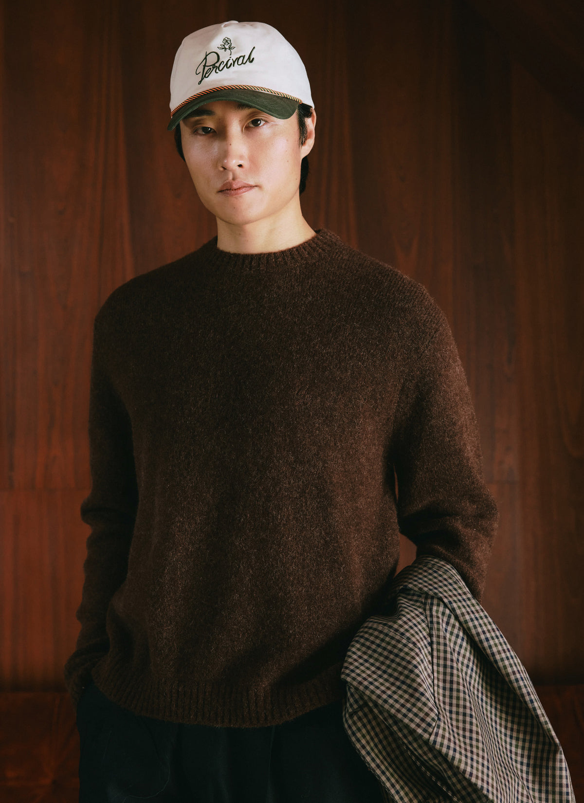 A model wears the Percival espresso mohair crew neck jumper and a cap in a studio shot.