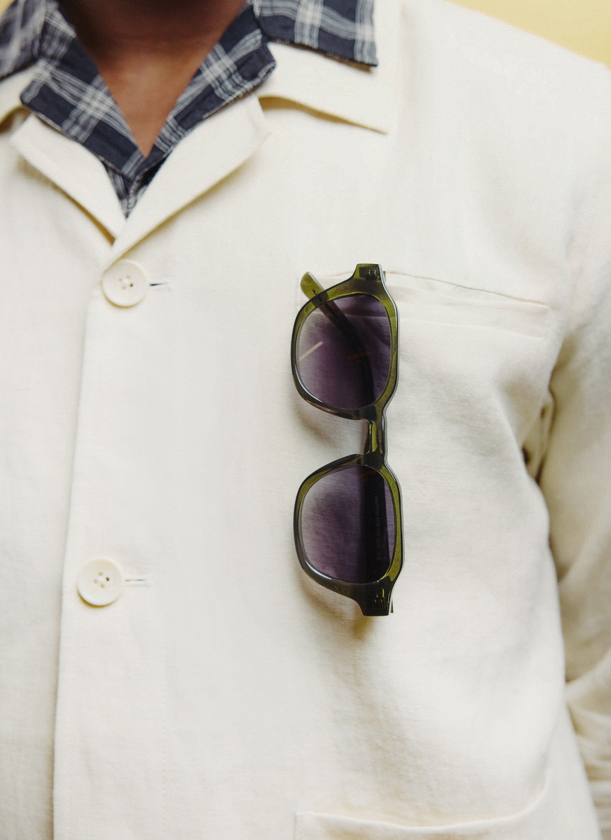 Close-up of the Percival olive green sunglasses, with light brown lenses, tucked into the pocket of a cream jacket.