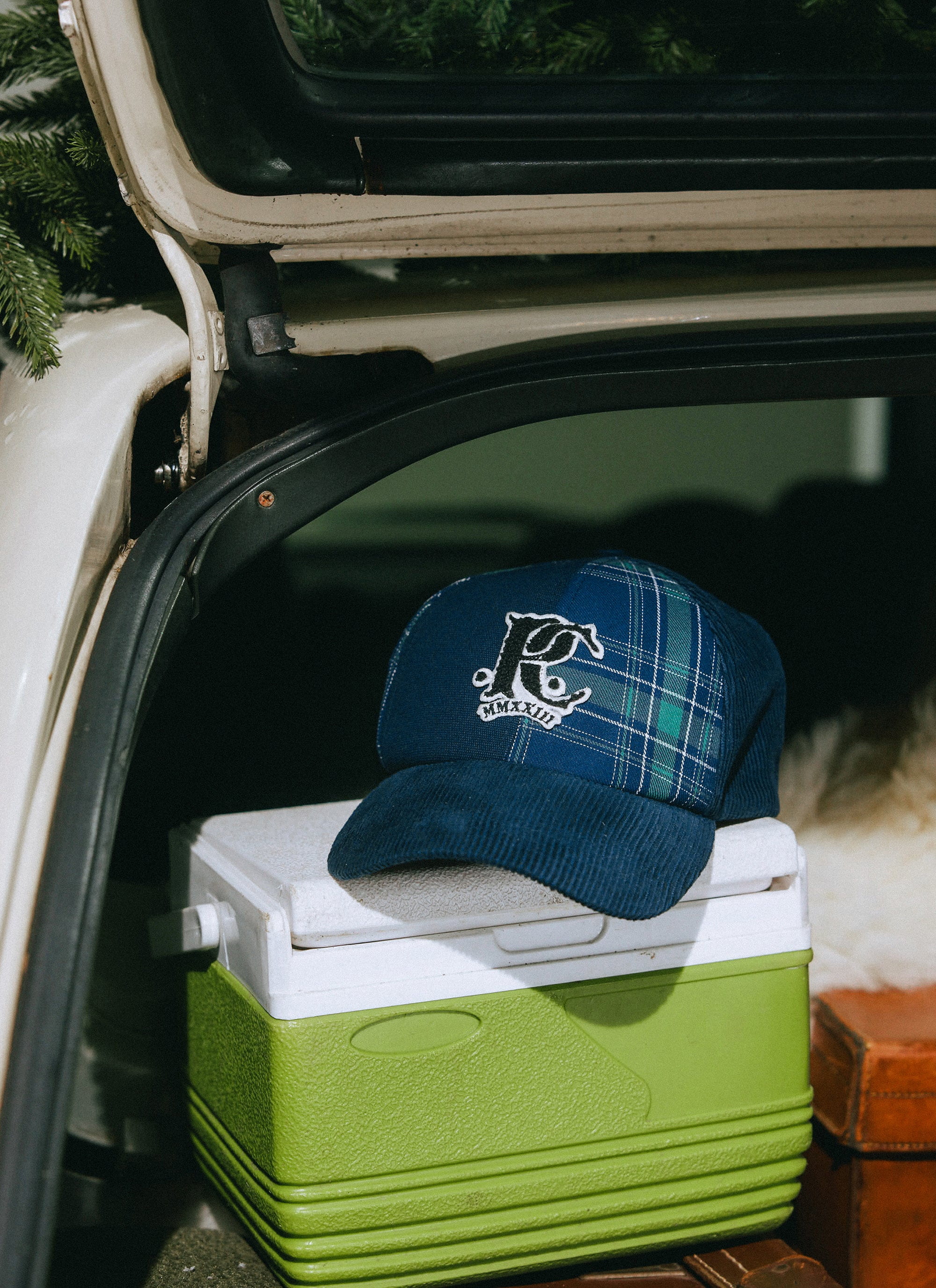 The Percival x Champion Cut and Sew Cap in multi cord and check panels, sitting on a cooler in the boot of a car.