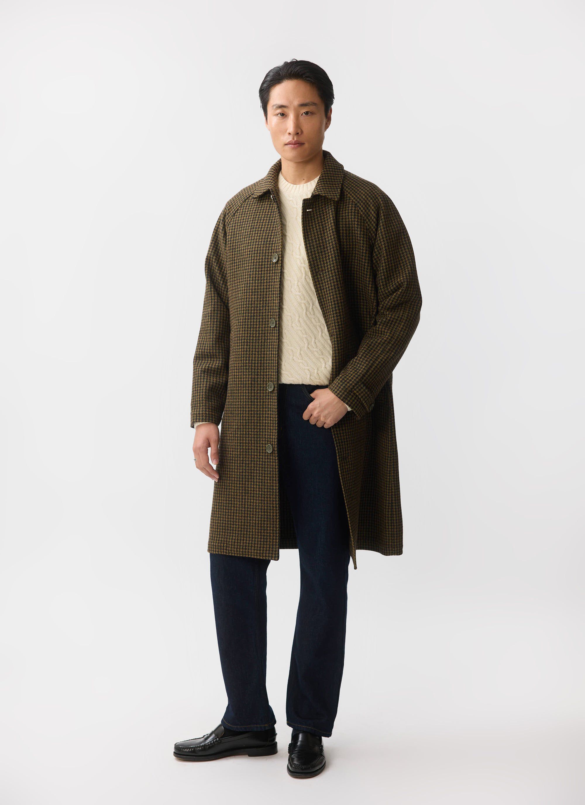 A man models the brown houndstooth wool Dickens Car Coat from Percival, layered over a cream jumper and dark jeans.