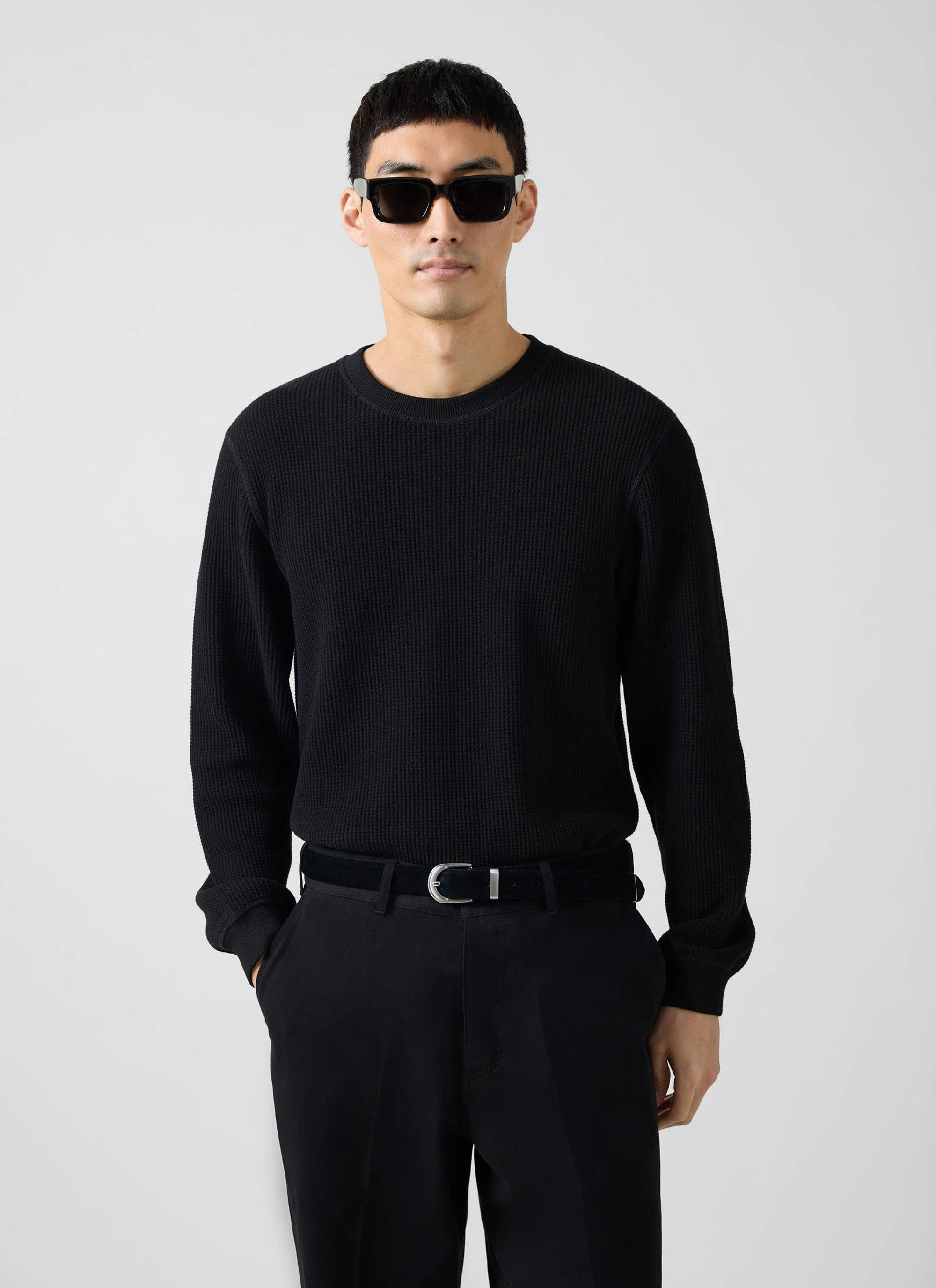 A man models the Percival black Waffle Long Sleeve T Shirt, styled with black trousers and sunglasses.