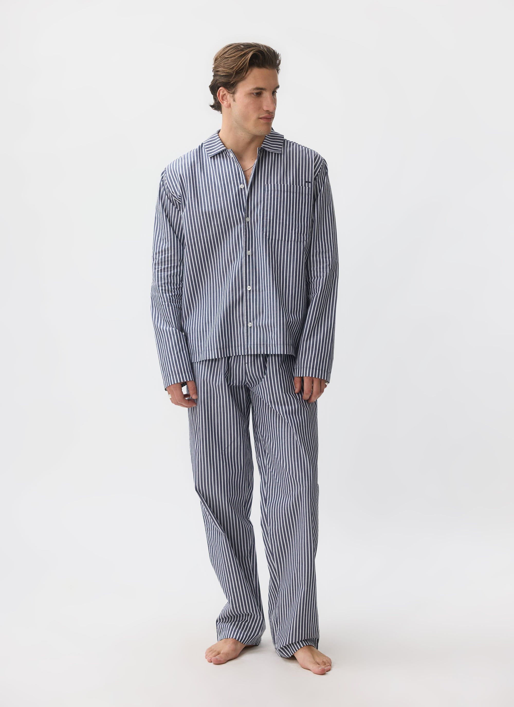 A model wears the Percival Pyjama Top and matching trousers in blue and white striped cotton against a white background.