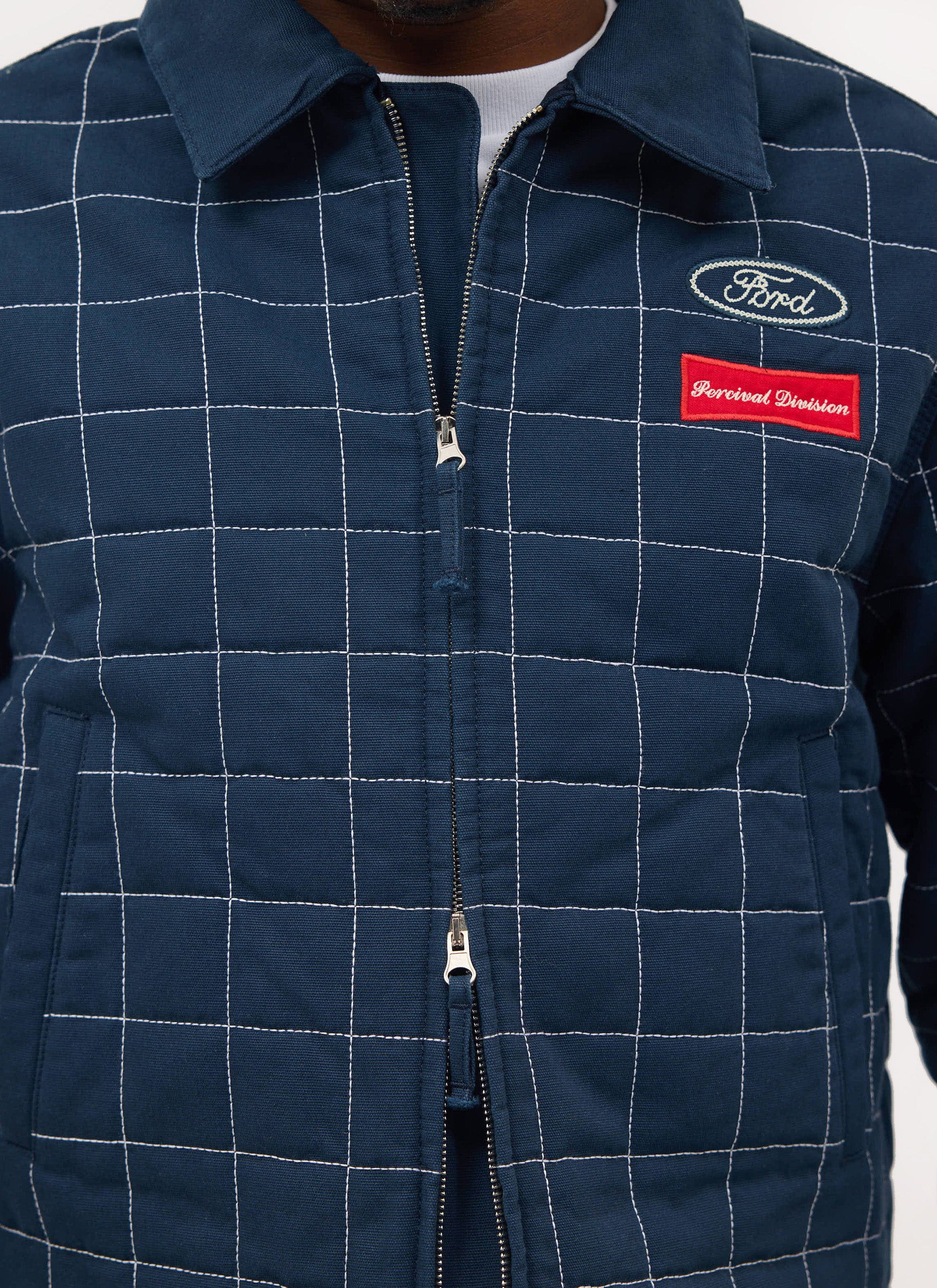 Close up shot of the navy quilted Percival x Ford Garage Harrington jacket showing the embroidered logos on the chest.