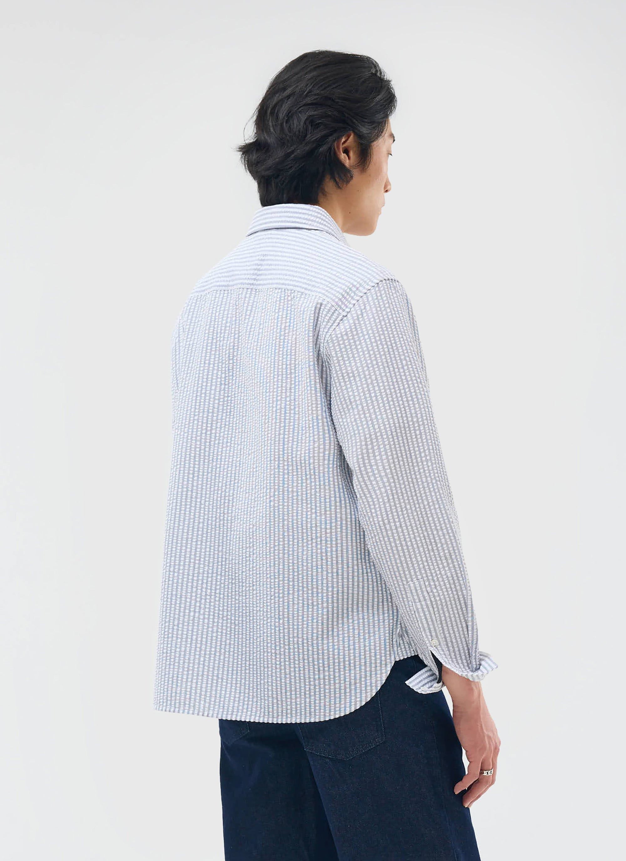 A model shows the back of the grey and ecru Percival Seersucker Stripe Pearce Shirt, showing its textured, oversized fit.