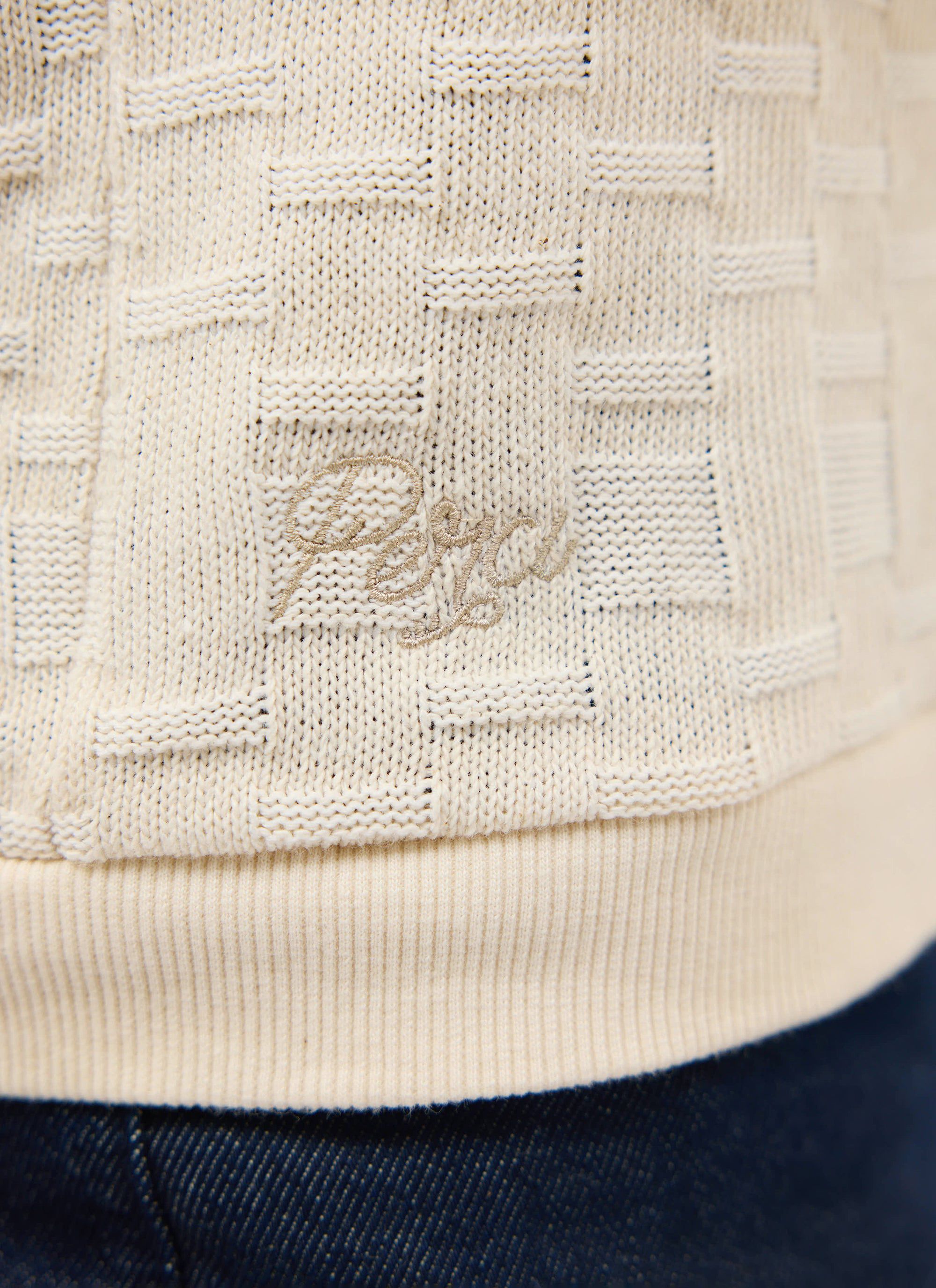 A close-up of the Percival Deck Negroni Knitted Shirt in ecru, highlighting the textured weave and tonal embroidered logo.