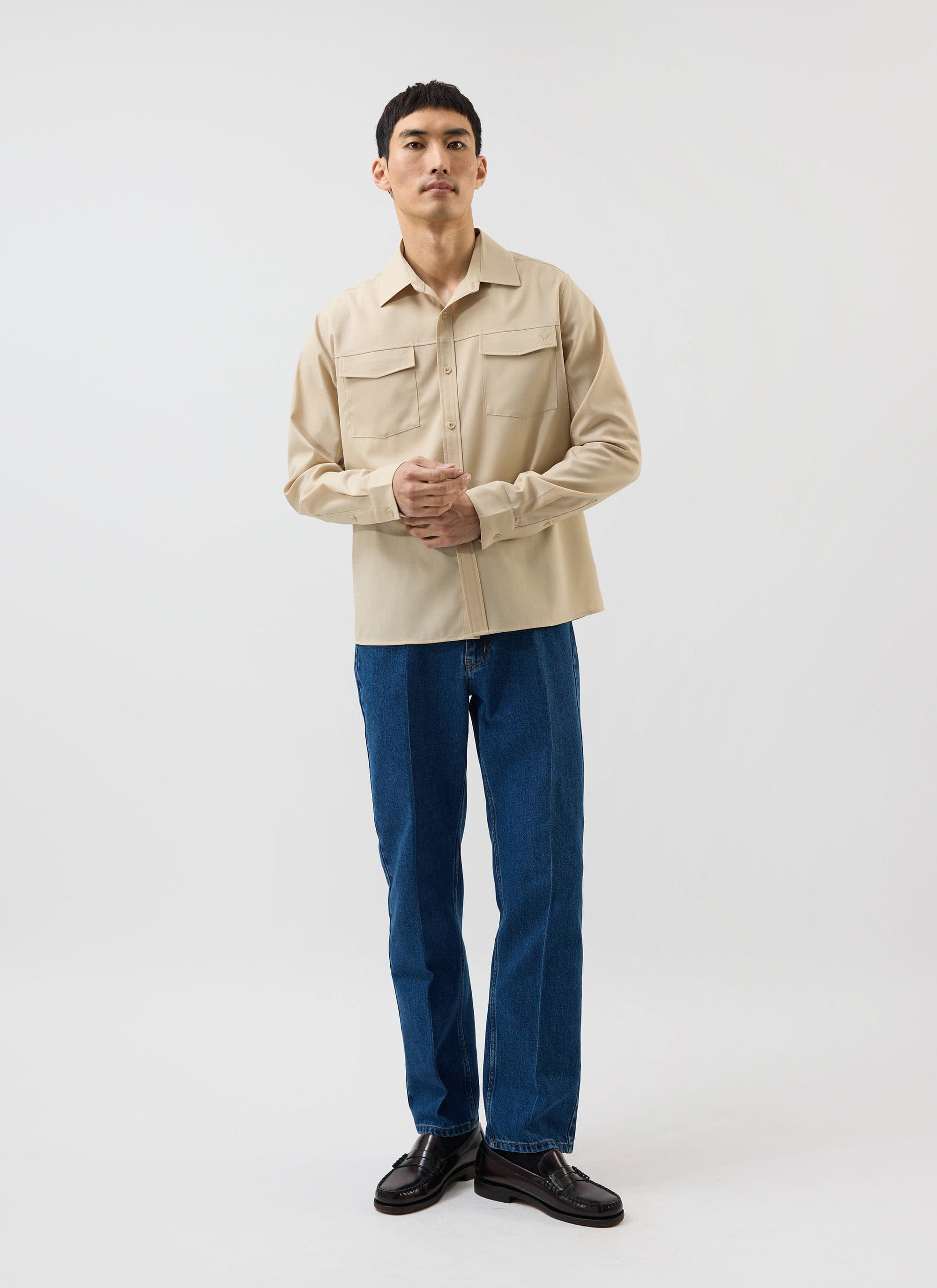 A model showcases the Percival x Warren Safari Long Sleeve Shirt in camel beige, paired with blue jeans and loafers.