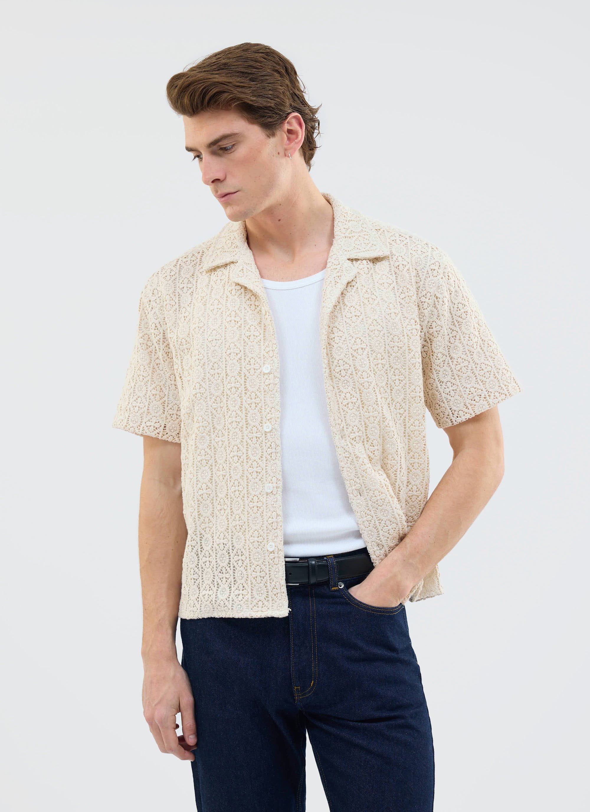 A model wears the Percival Elio Crochet Cuban Shirt in ecru, layered over a white vest with dark blue jeans.