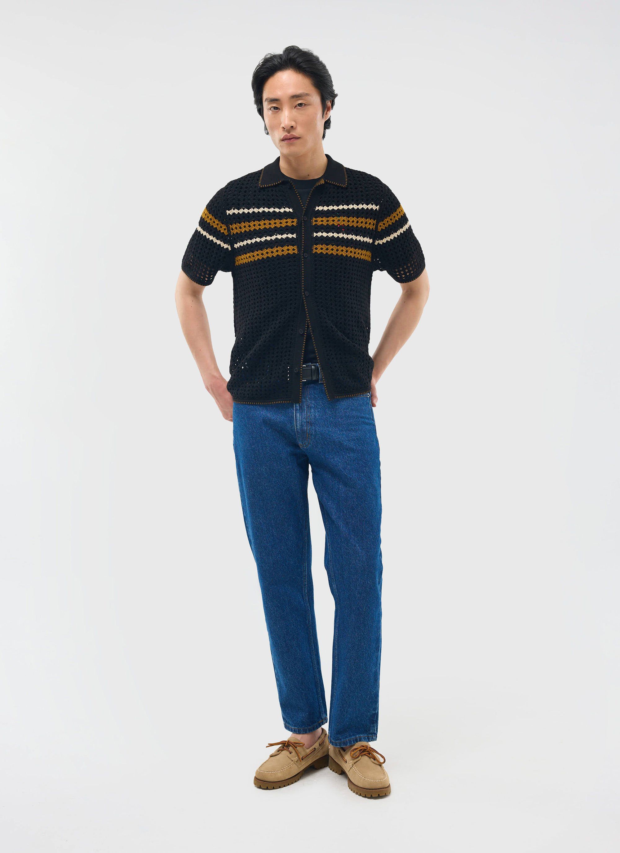 A model wears the black Percival Pesaro Knitted Shirt, a crochet design with stripes, styled with blue jeans.